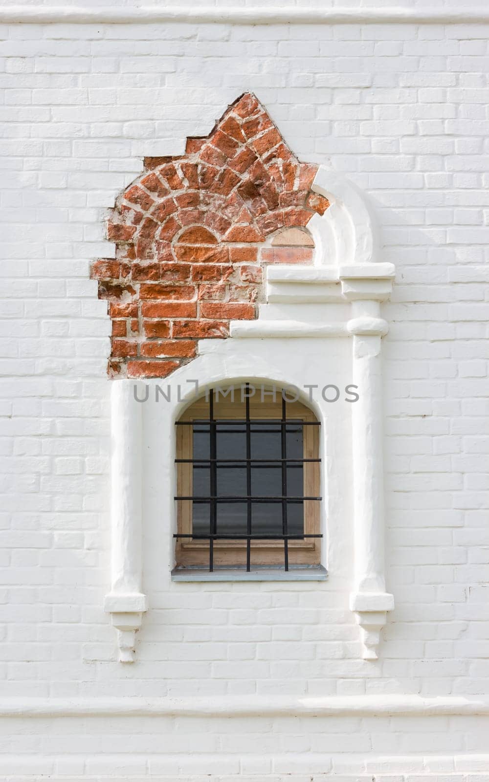 Rostov Veliky, Russia - September 13, 2021: close-up of a figured window with iron bars in the ancient restored white brick wall of the Stable Yard - part of the Rostov Kremlin. Medieval historical background.