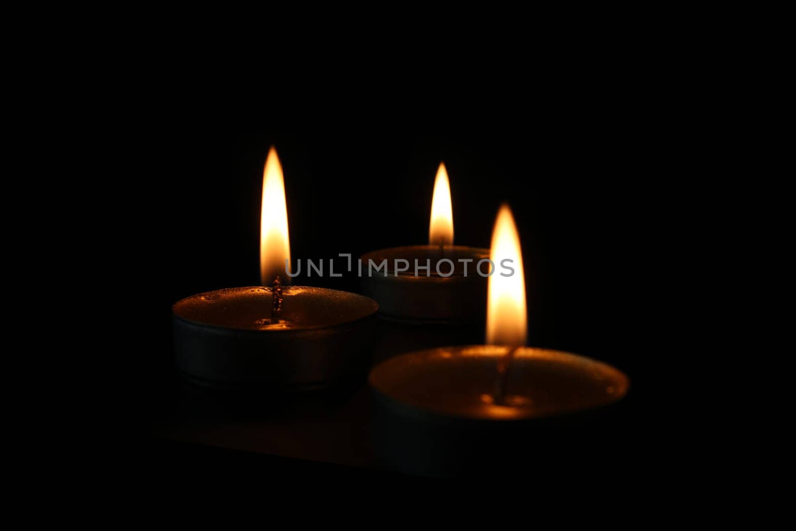 Three burning candles close-up on a black background with copy space. Blurred foreground and background.