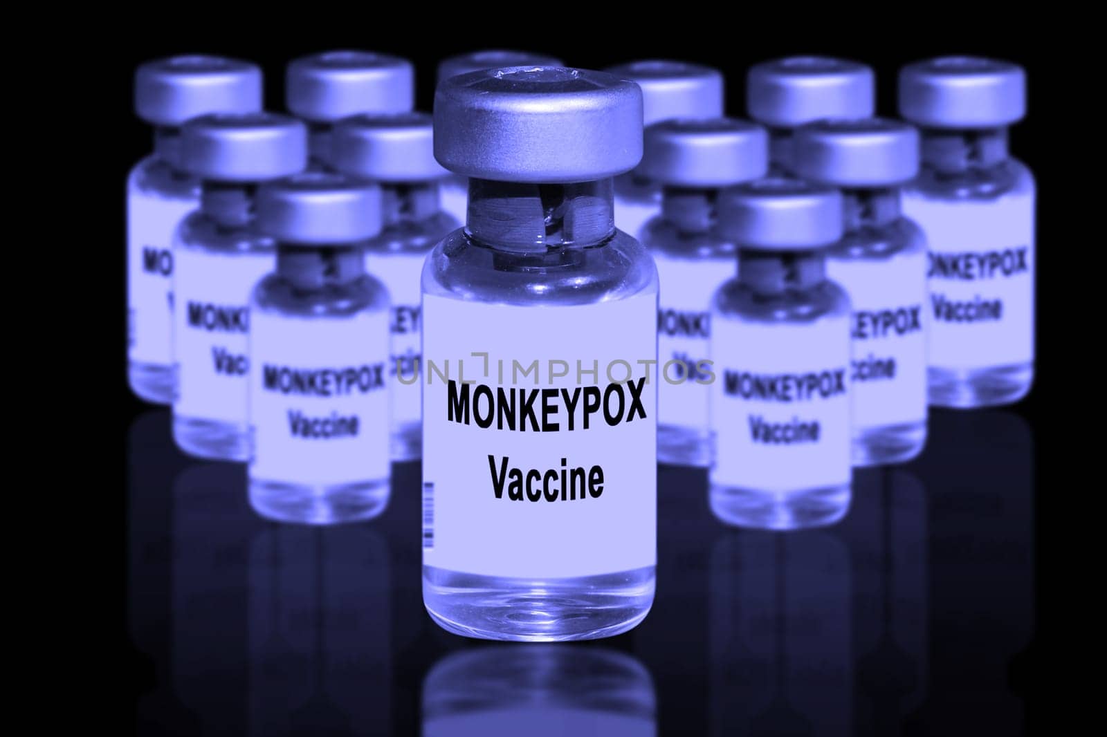 Monkeypox vaccine close-up on a black mirror background. In the background are blurred vaccine vials.