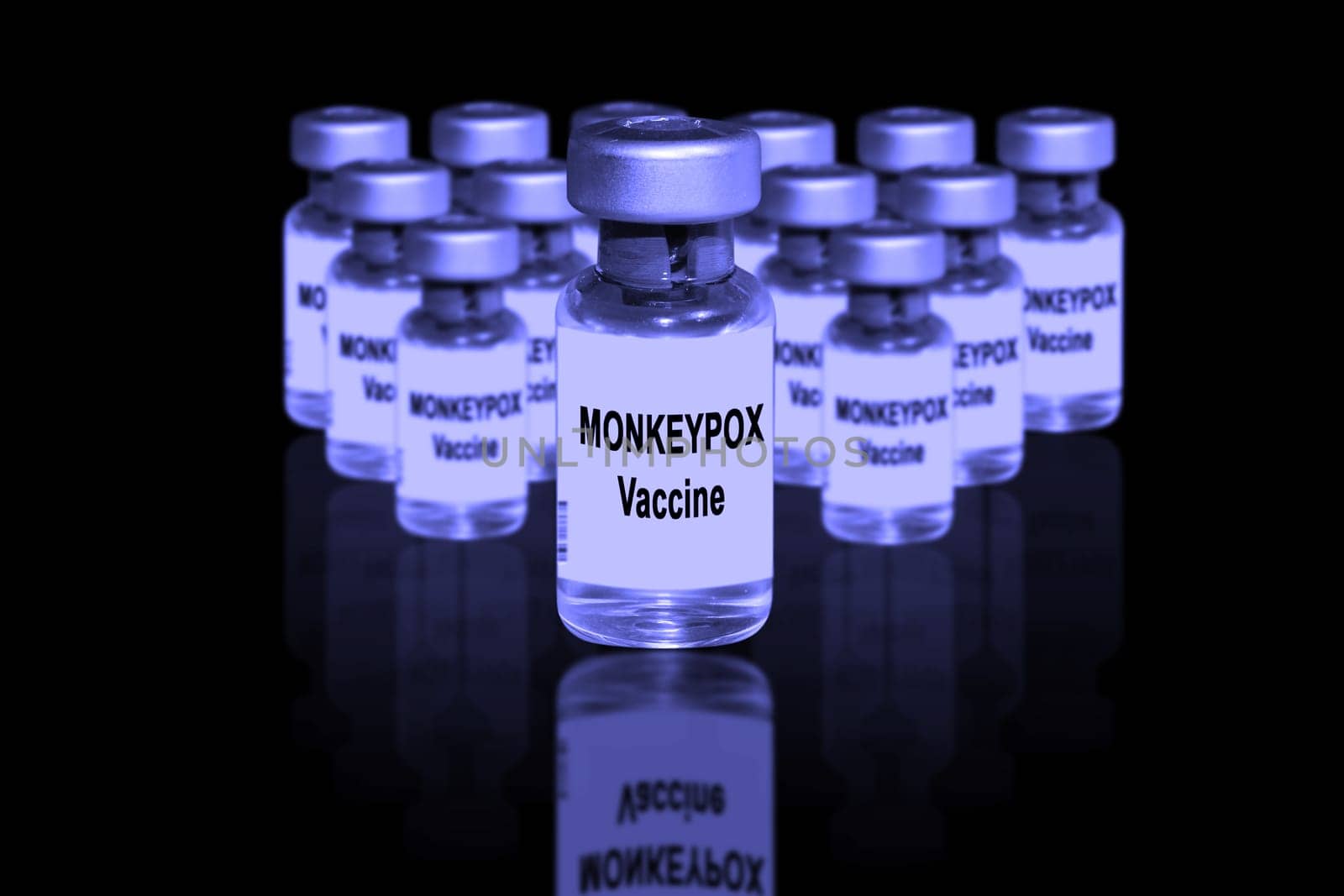 Monkeypox vaccine close-up on a black mirror background. In the background are blurred vaccine vials.