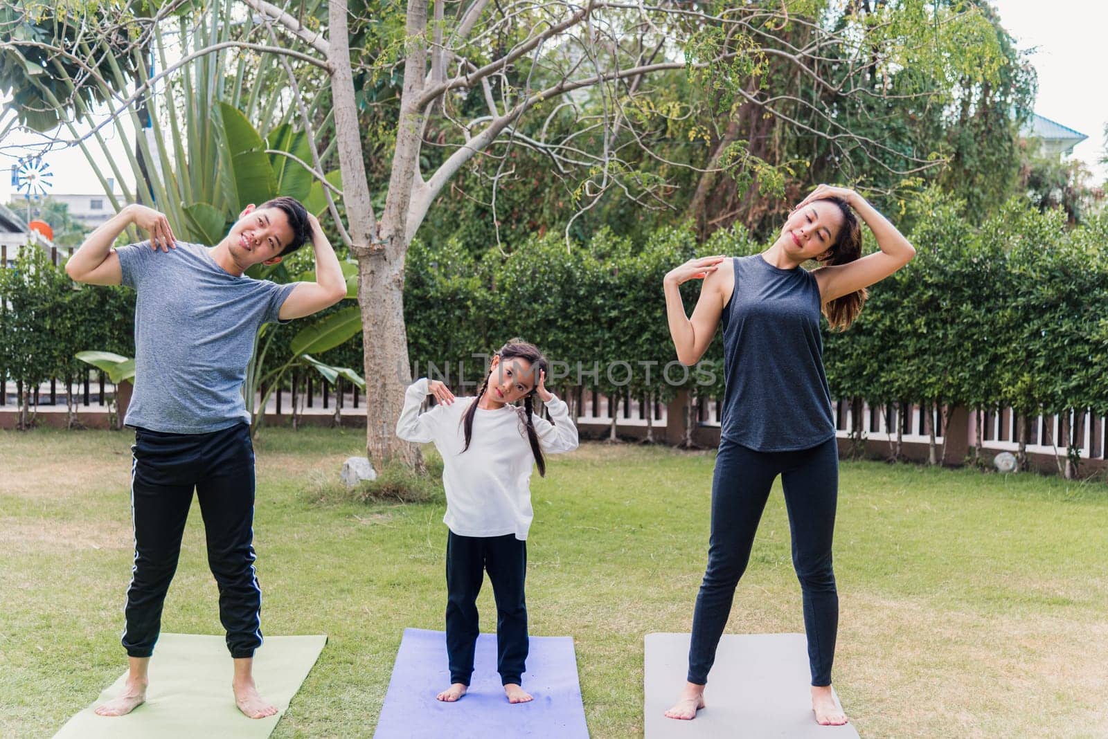 Asian young mother, father and child daughter practicing exercising stretching together before yoga workout outdoor morning in nature a field garden park. Happy family kid sport healthy lifestyle
