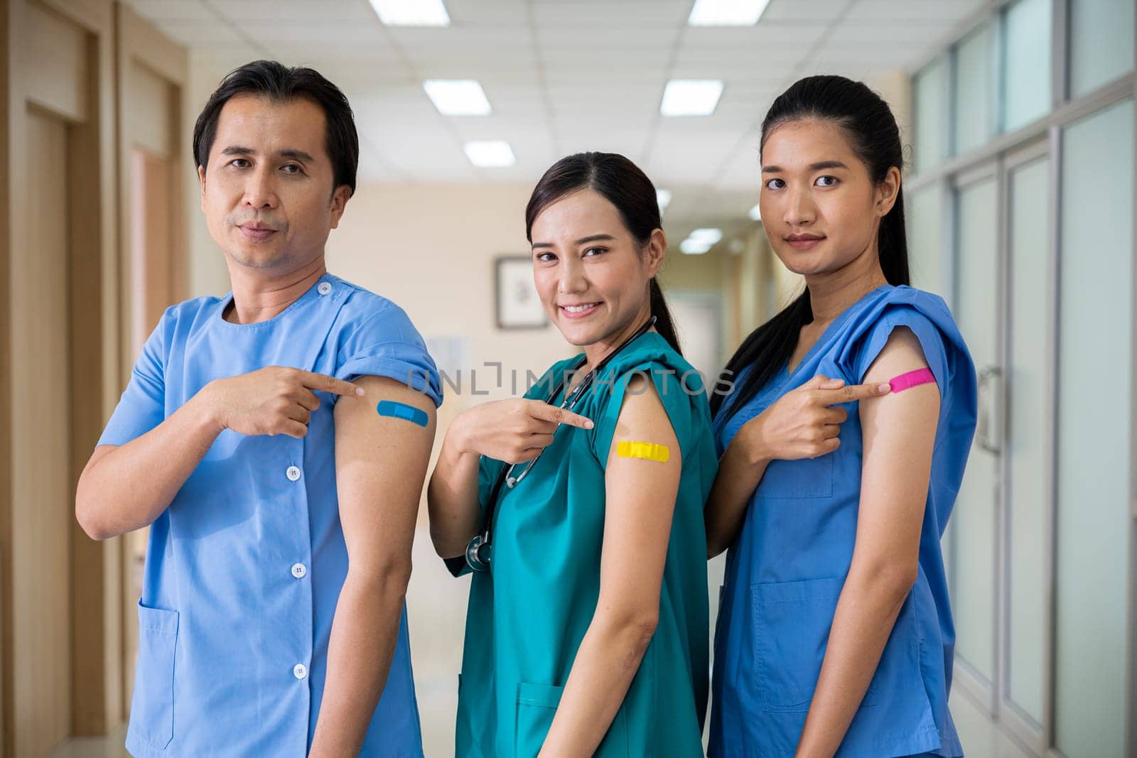 Medical personnel pointing to bandage with plaster on arm after getting against Covid-19 vaccine, happy nurse woman and man standing at hospital, Covid-19 vaccination concept