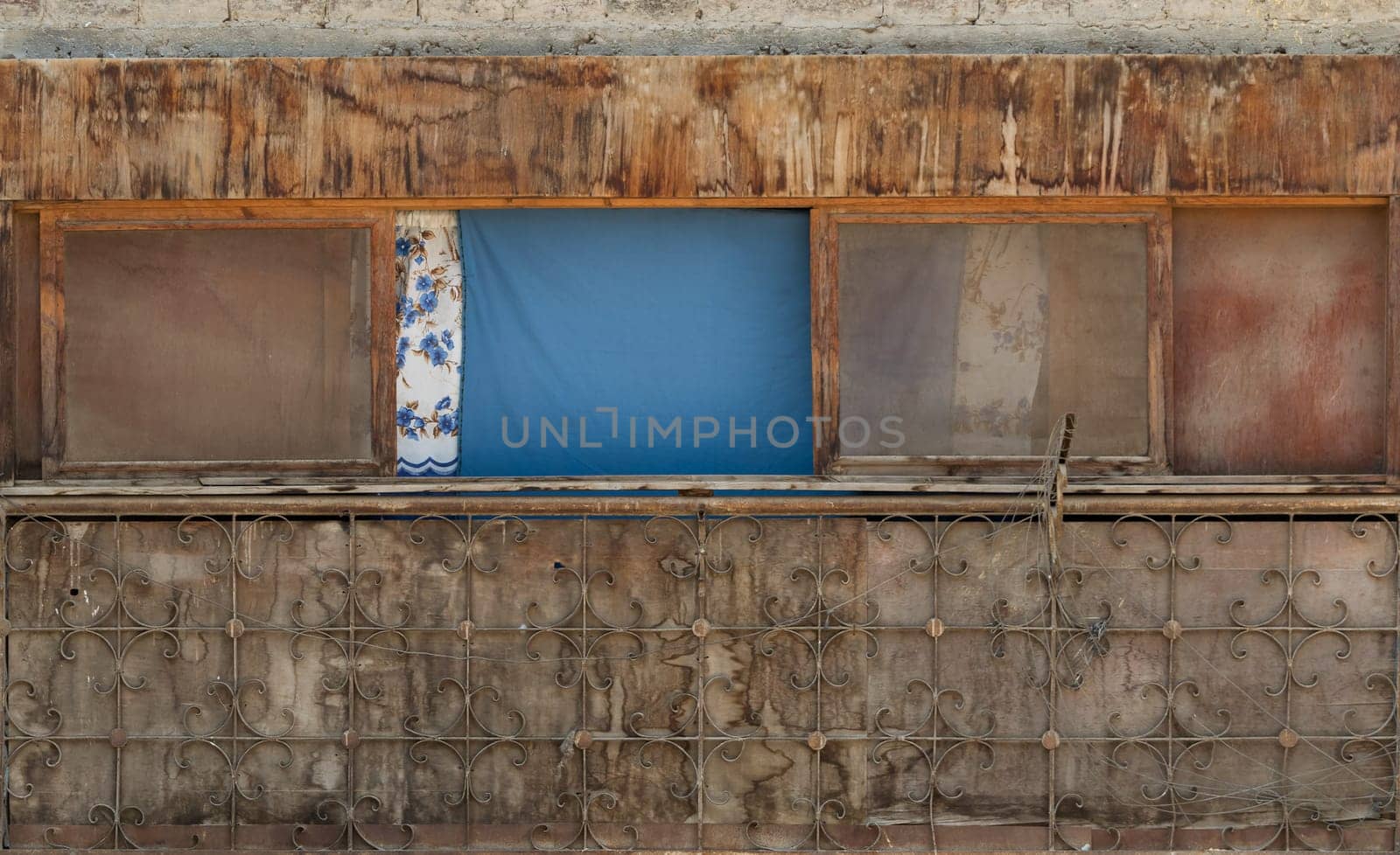 Exterior of old weathered shack with dirty windows and cloth curtains on sunny day in village