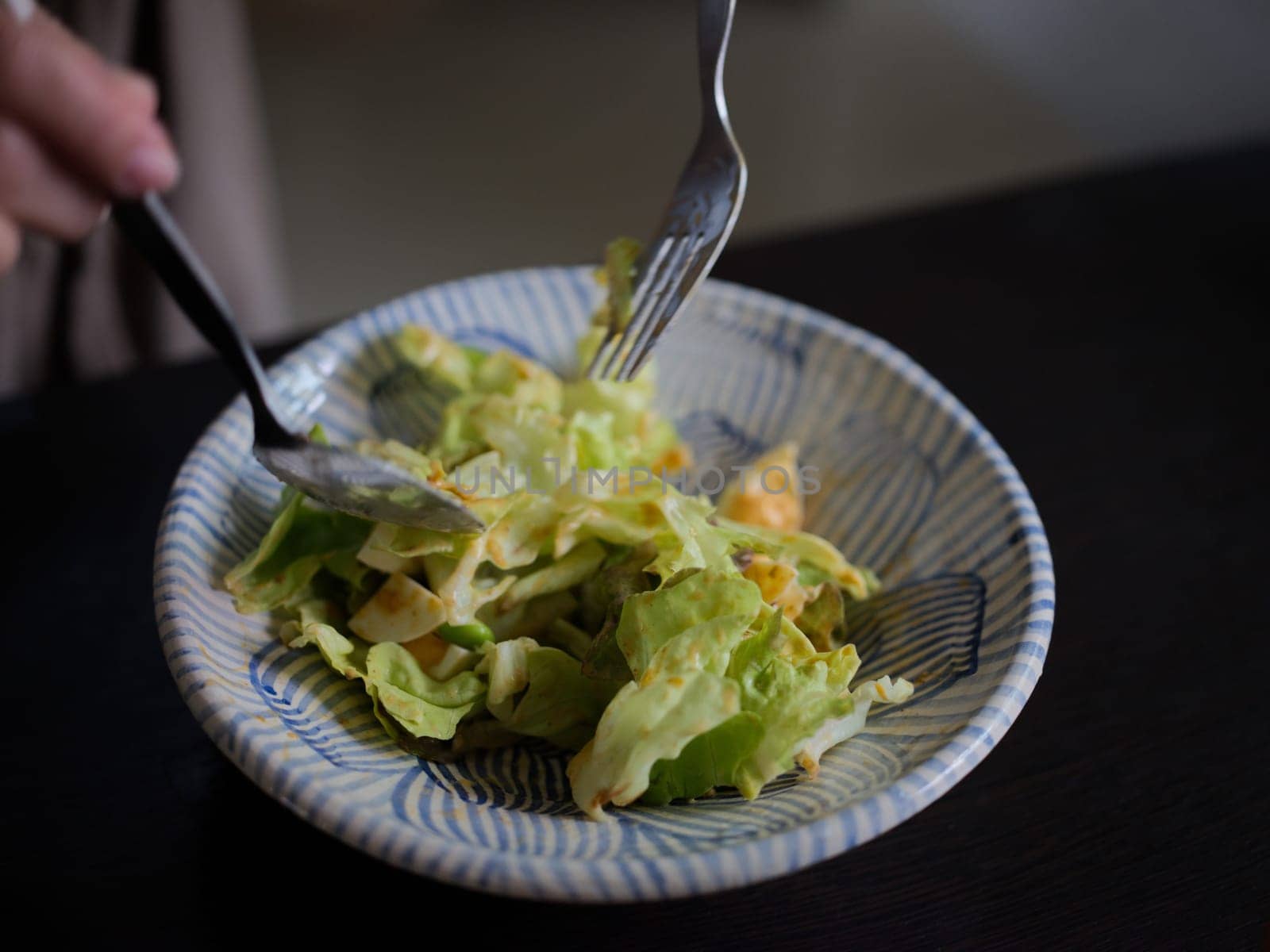 Woman mixing delicious food salad ingredients with spoons in kitchen