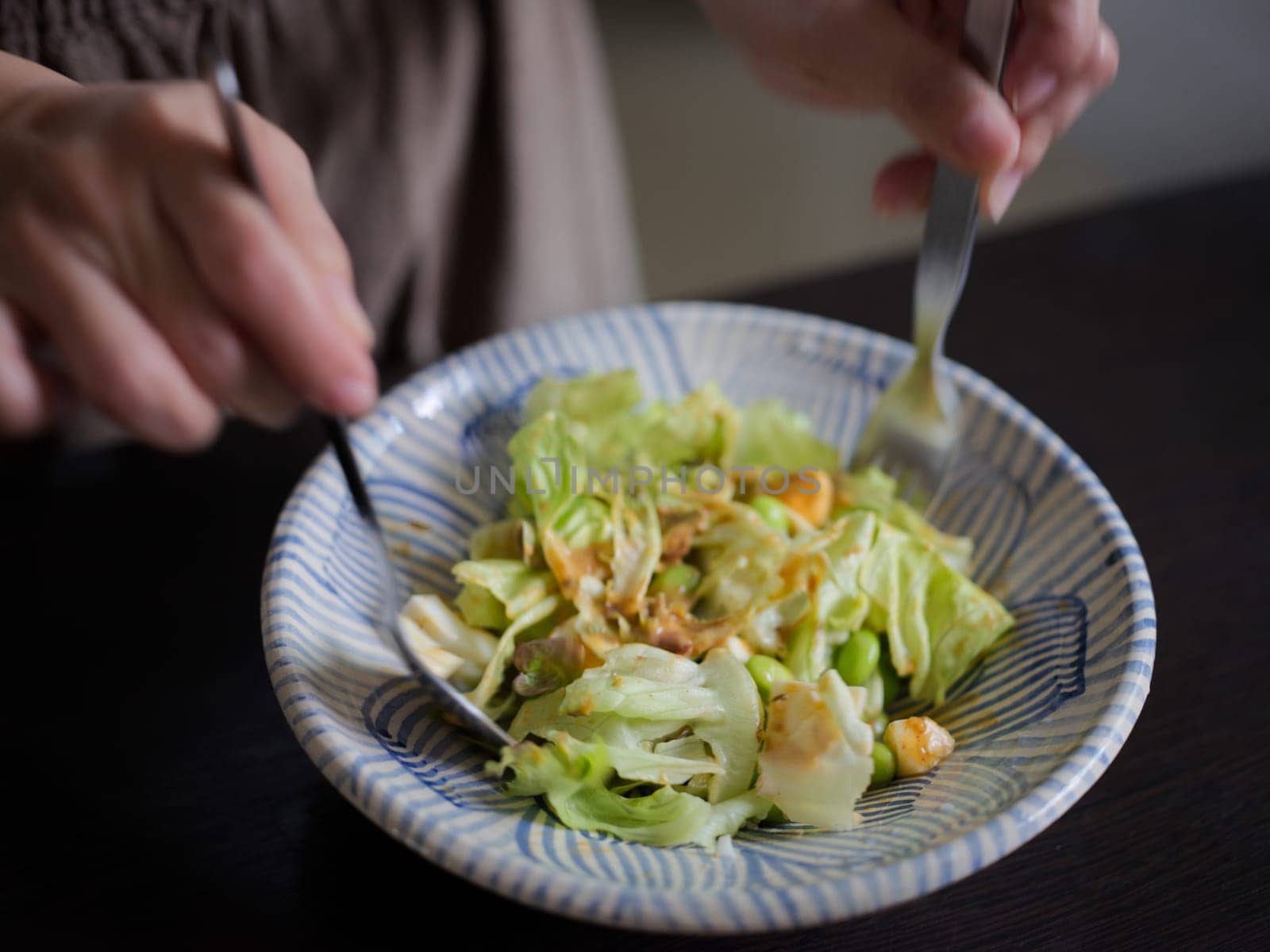 Woman mixing delicious food salad ingredients with spoons in kitchen
