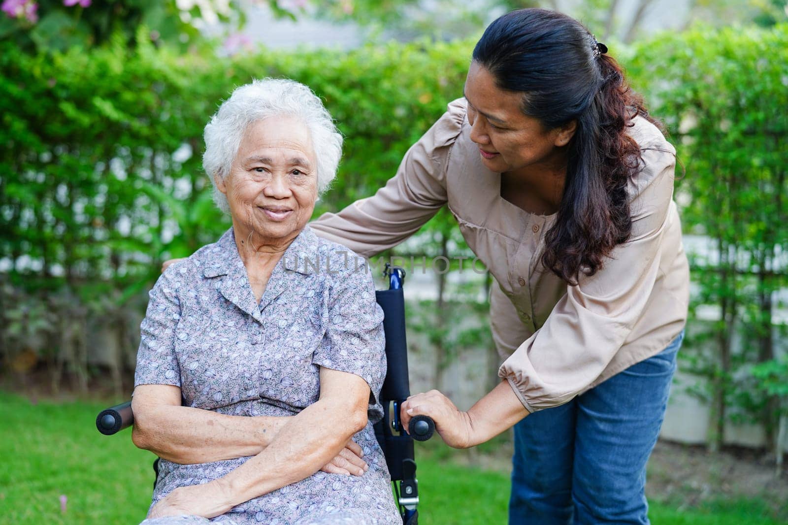 Caregiver help Asian elderly woman disability patient sitting on wheelchair in park, medical concept.