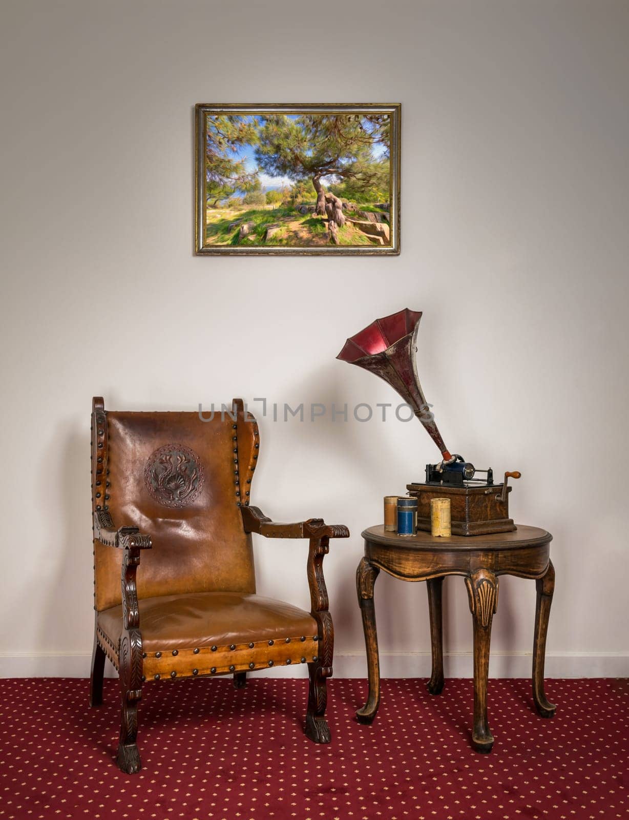 Retro ornate armchair, a 1911 old phonograph with three cylinder records on round coffee table and hanged painting on red carpet