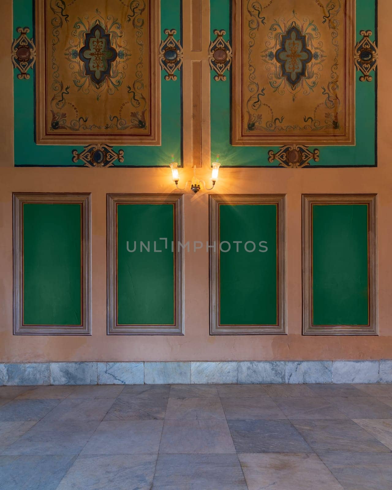 Beautiful elegant carved green frames on orange wall with ornate border and lanterns over white marble tiled floor, in abandoned old building