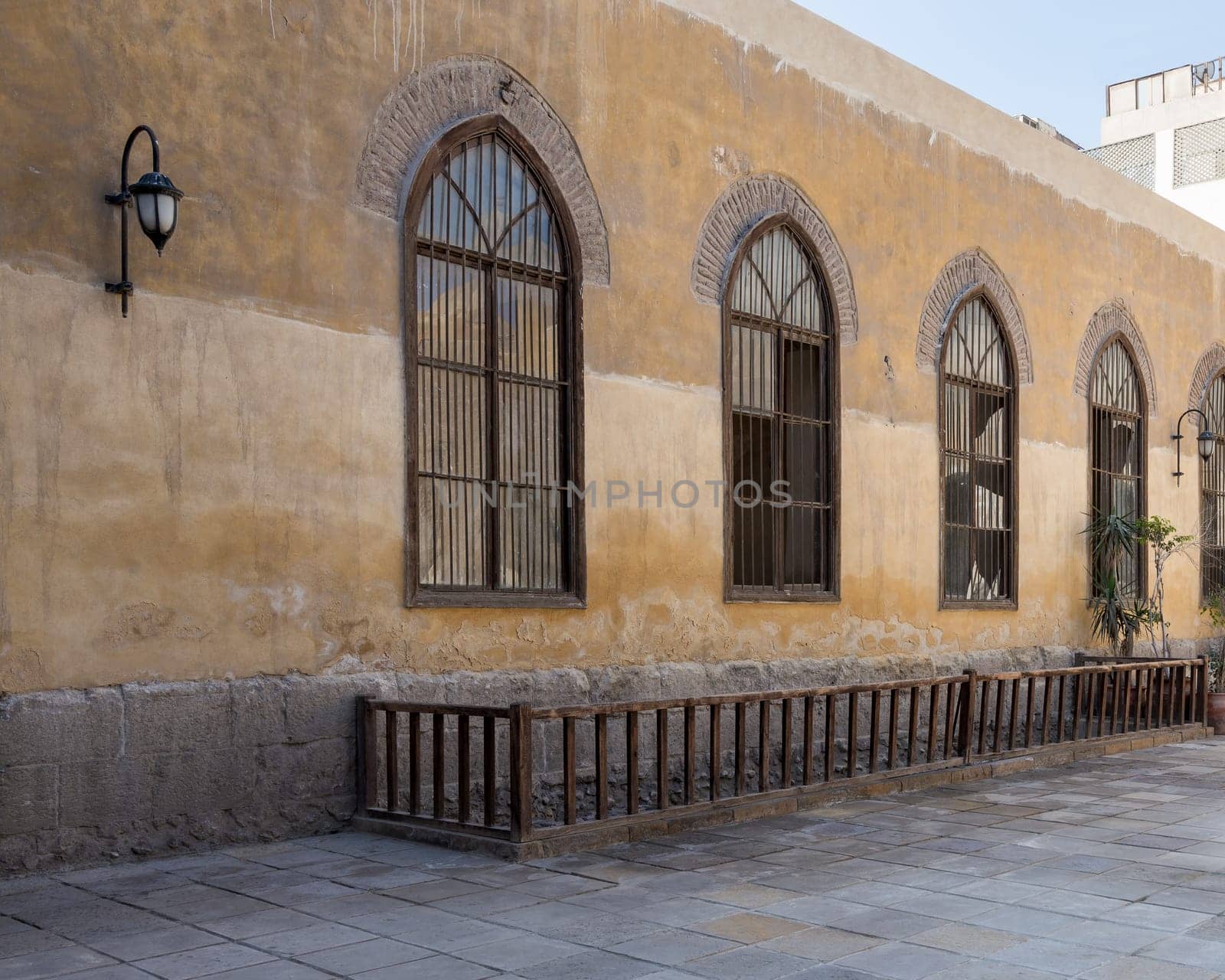 Row of three adjacent wooden grunge arched window with decorated wrought iron grid over yellow stone bricks wall and wooden balustrade, Medieval Cairo, Egypt