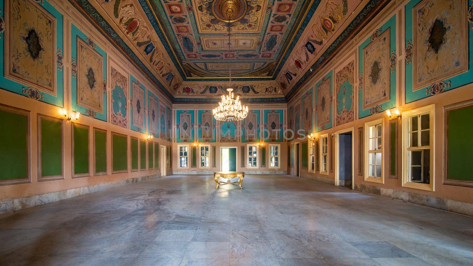 Royal era historic Manasterly Palace with beautiful elegant carved frames on green wall with ornate borders, floral decorated ceiling, chandelier, narrow windows, and marble floor, Cairo, Egypt