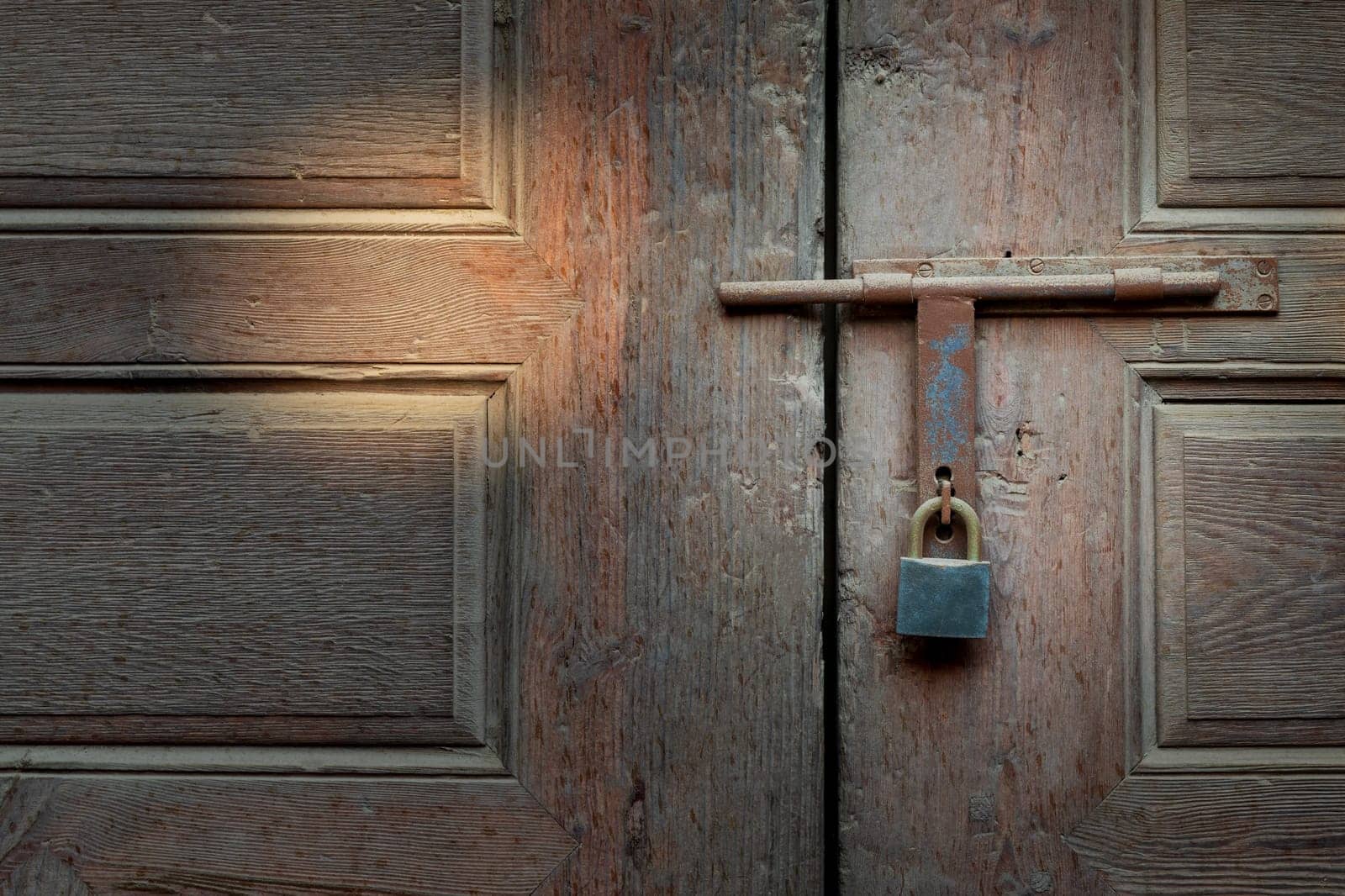 Closeup of rusted metal aged latch and padlock over weathered wooden door