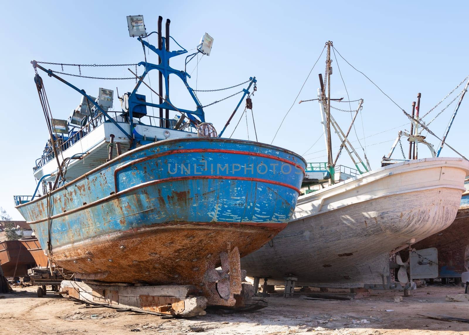 Old rusty vessels under repairing located on grungy dry dock in shipyard against blue sky on sunny day in old shipbuilding plant