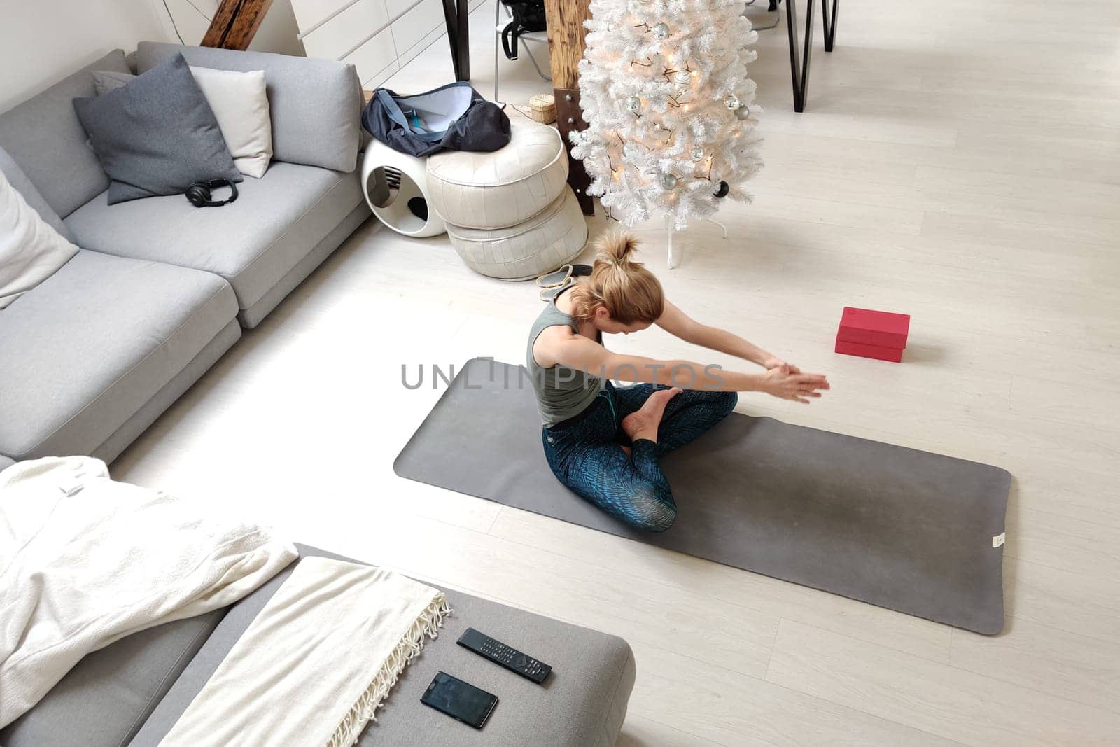 Beautiful blonde woman doing home workout indoors. Woman practice yoga at home. Fit girl using workout tutorials for healthy active lifestyle. Woman using quarantine for home workouts and stretching