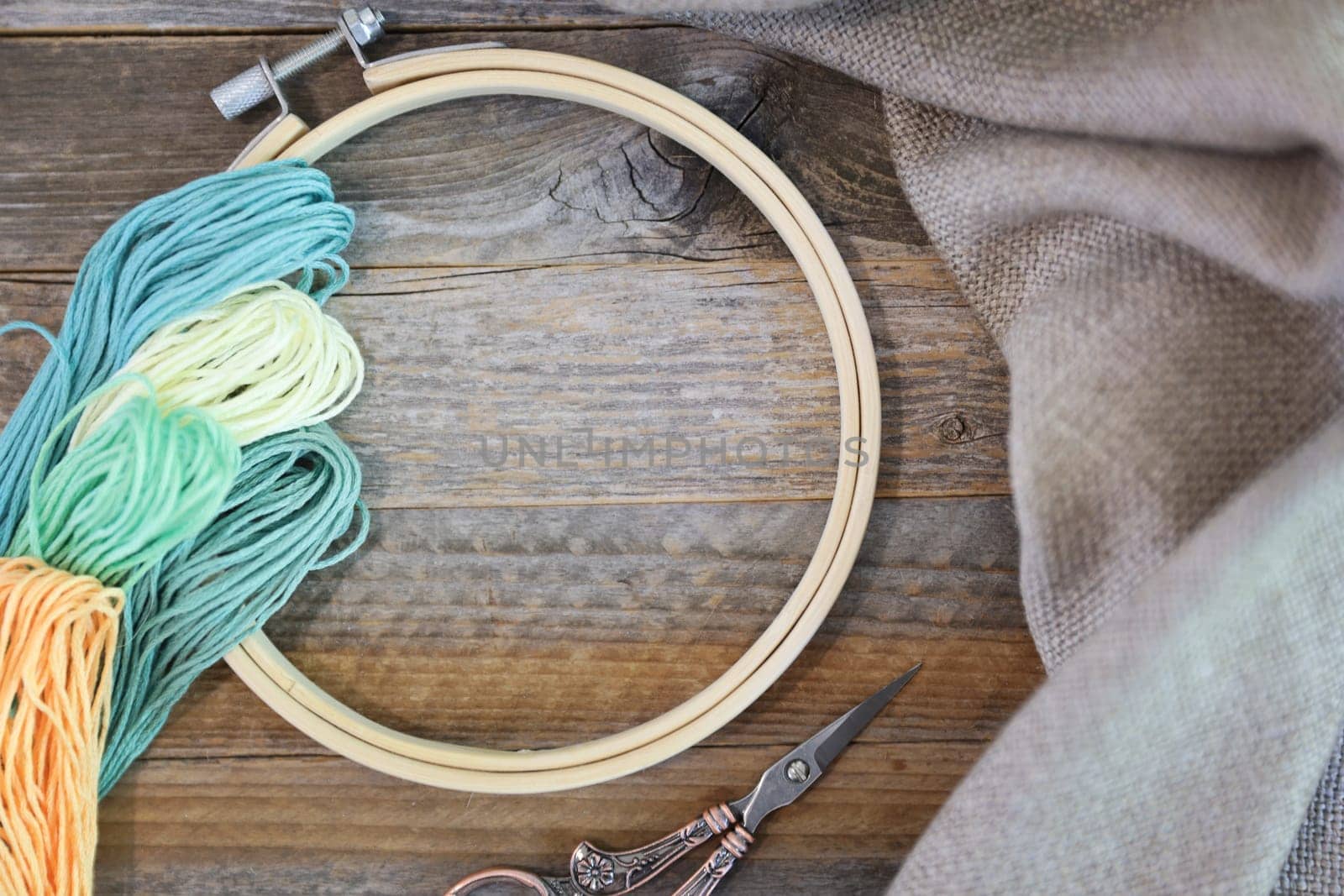 Bobbins of colorful embroidery floss with hoop and sissors on rustic wooden table. Flat lay with copy space in center of hoop