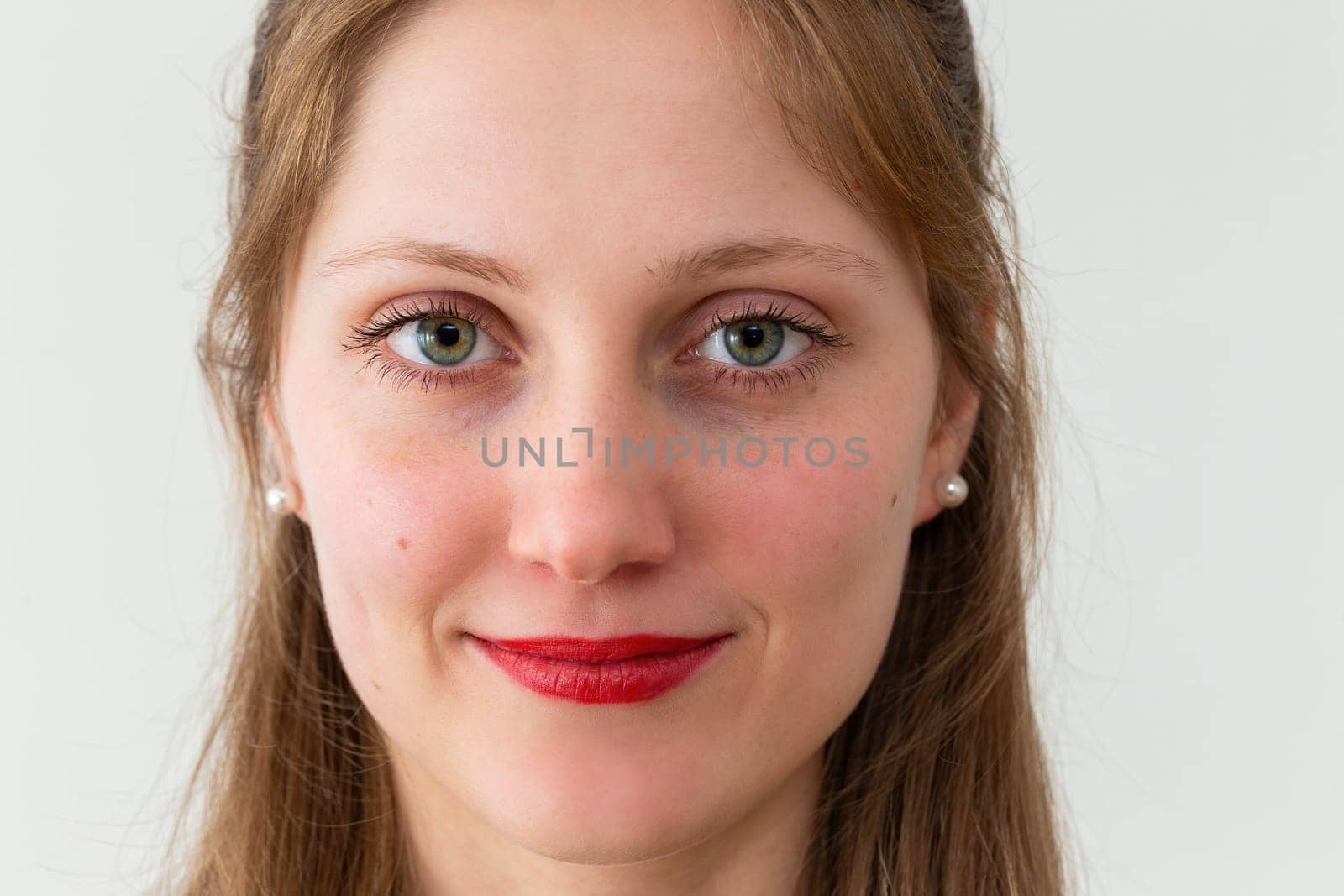 Portrait of smiling young woman looking to the camera in office with white background. Female human looking into the camera in horizontal composition.