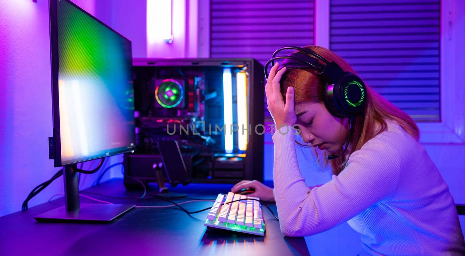 Game over. Angry Asian gamer wearing gaming headphones playing joystick console video game on computer PC neon light at home feeling sad disappointed about game losing, tournament player E-Sport