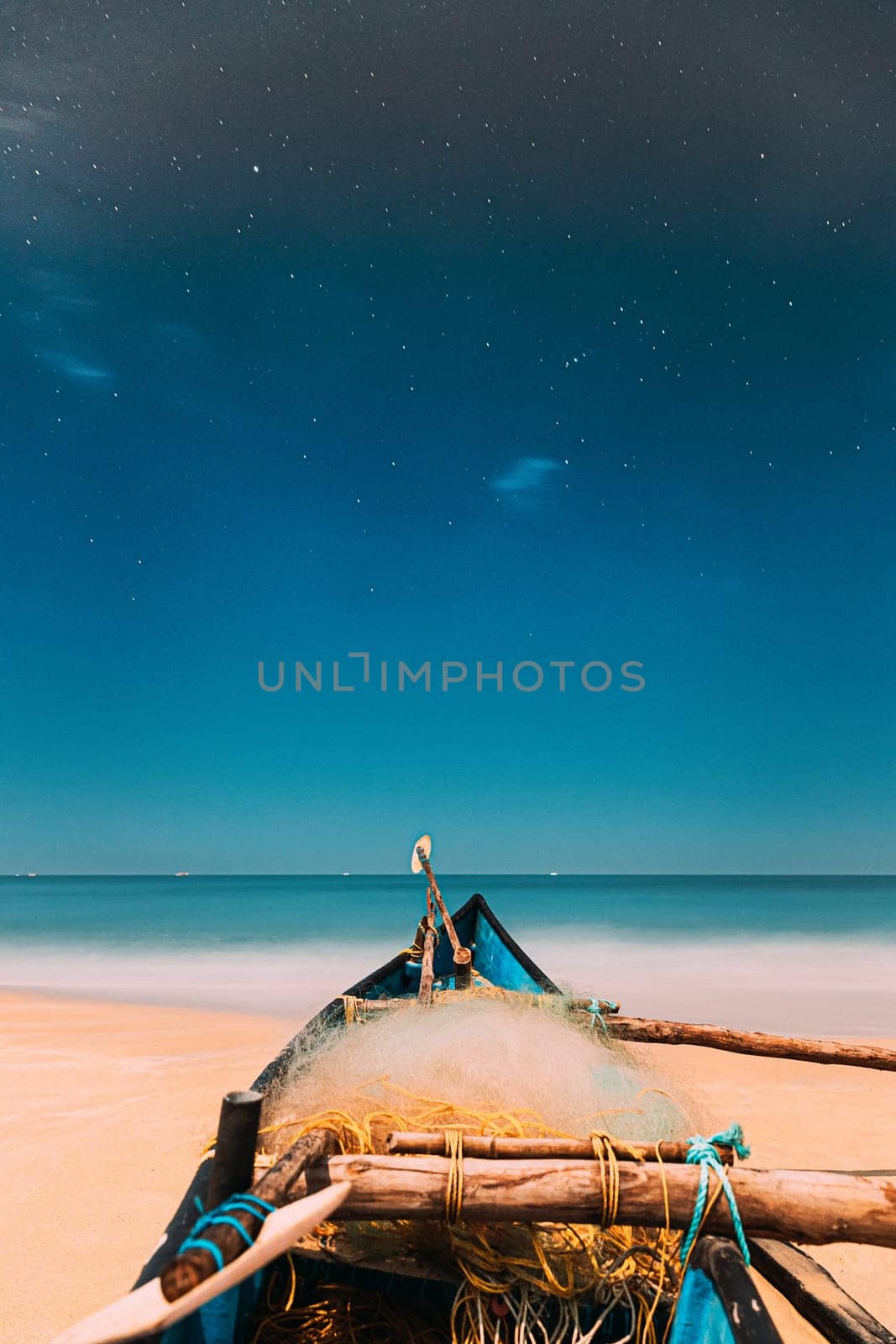 Goa, India. Real Night Sky Stars. Natural Starry Sky Blue Color Above Sea Seascape Ocean Beach. Background. Parked Old Wooden Boat At Coast.