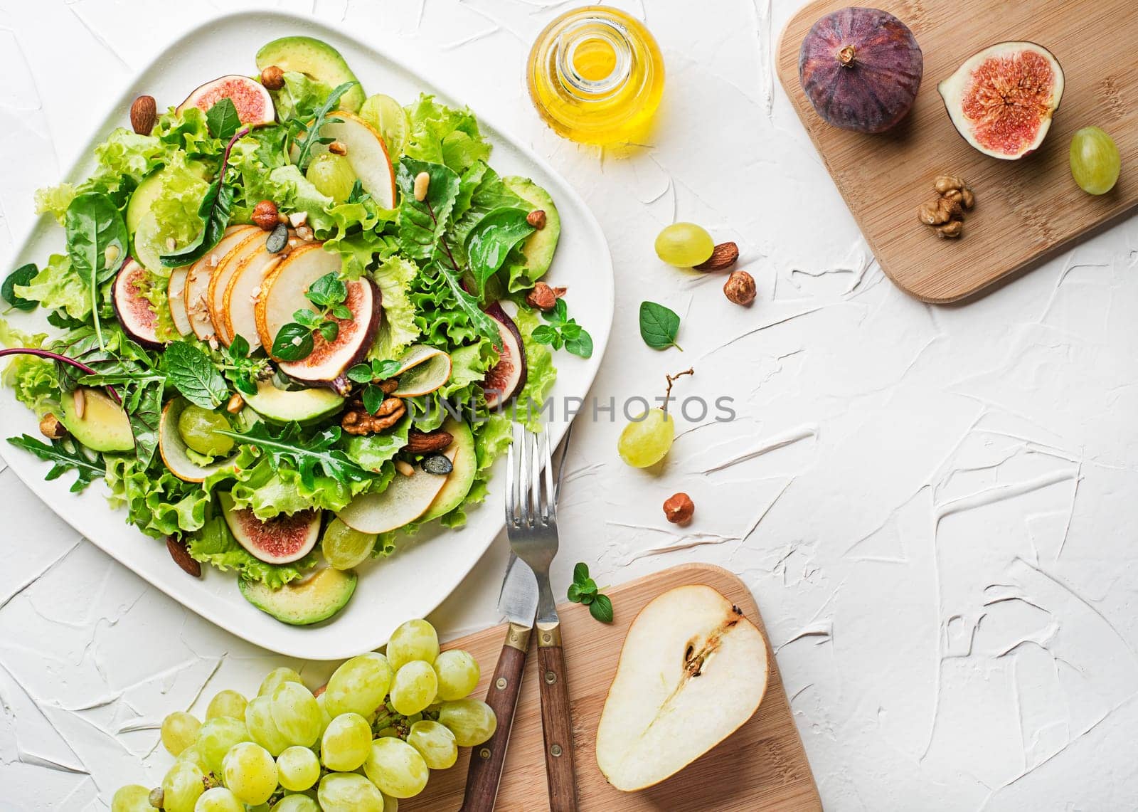 Fresh green leafy salad with fruits and nuts on white table background. Concept for a tasty and healthy meal