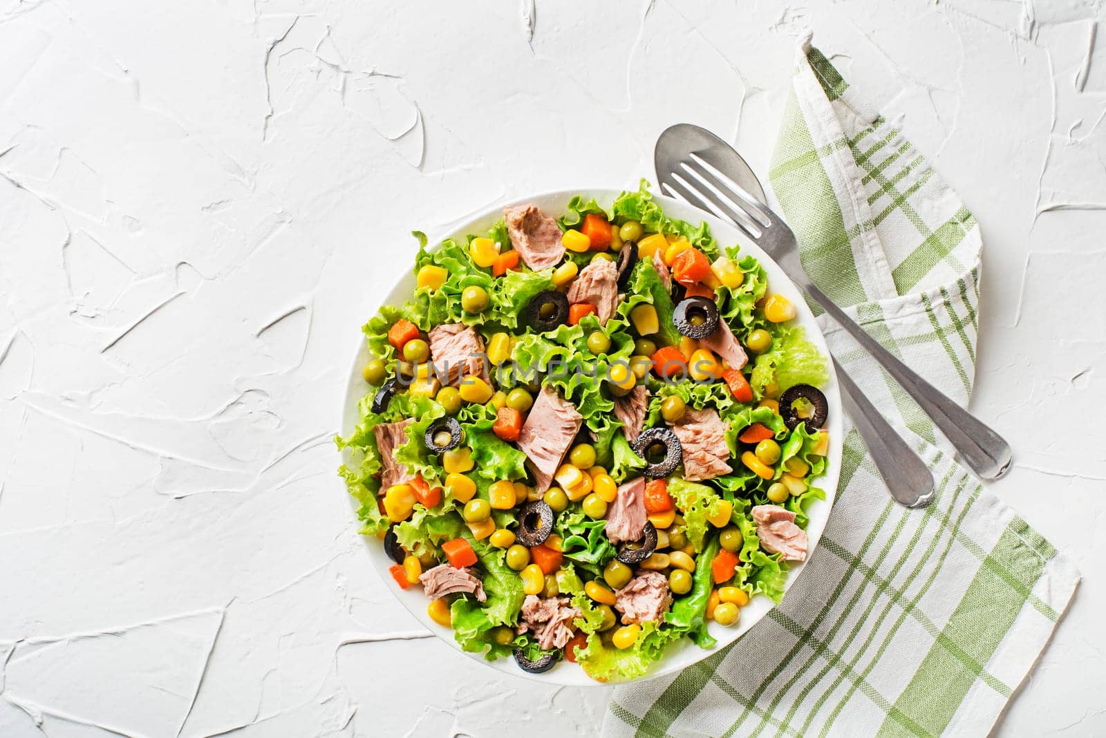 Healthy Green salad with tuna, corn, carrots, peas, and olives on white table background. Mexican corn salad.