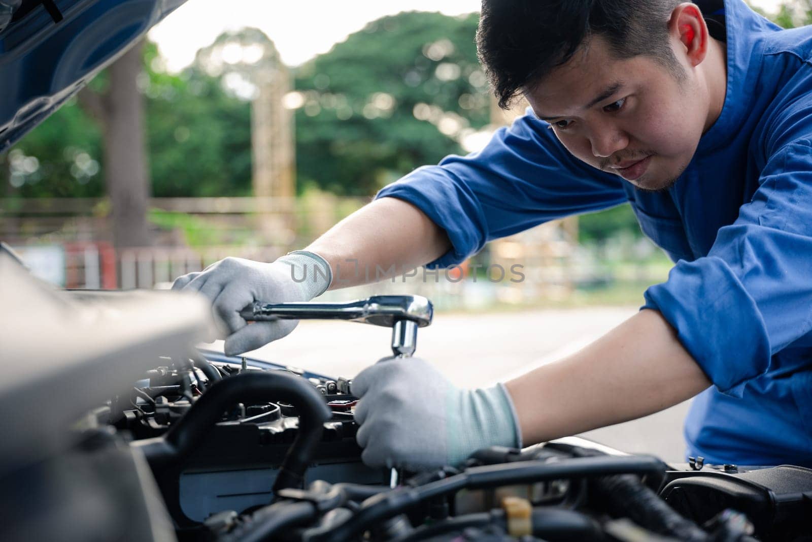 Service outdoor. Asian auto mechanic man working on car engine using wrench to repair and maintenance, broken car care check and fixed the problem and services insurance