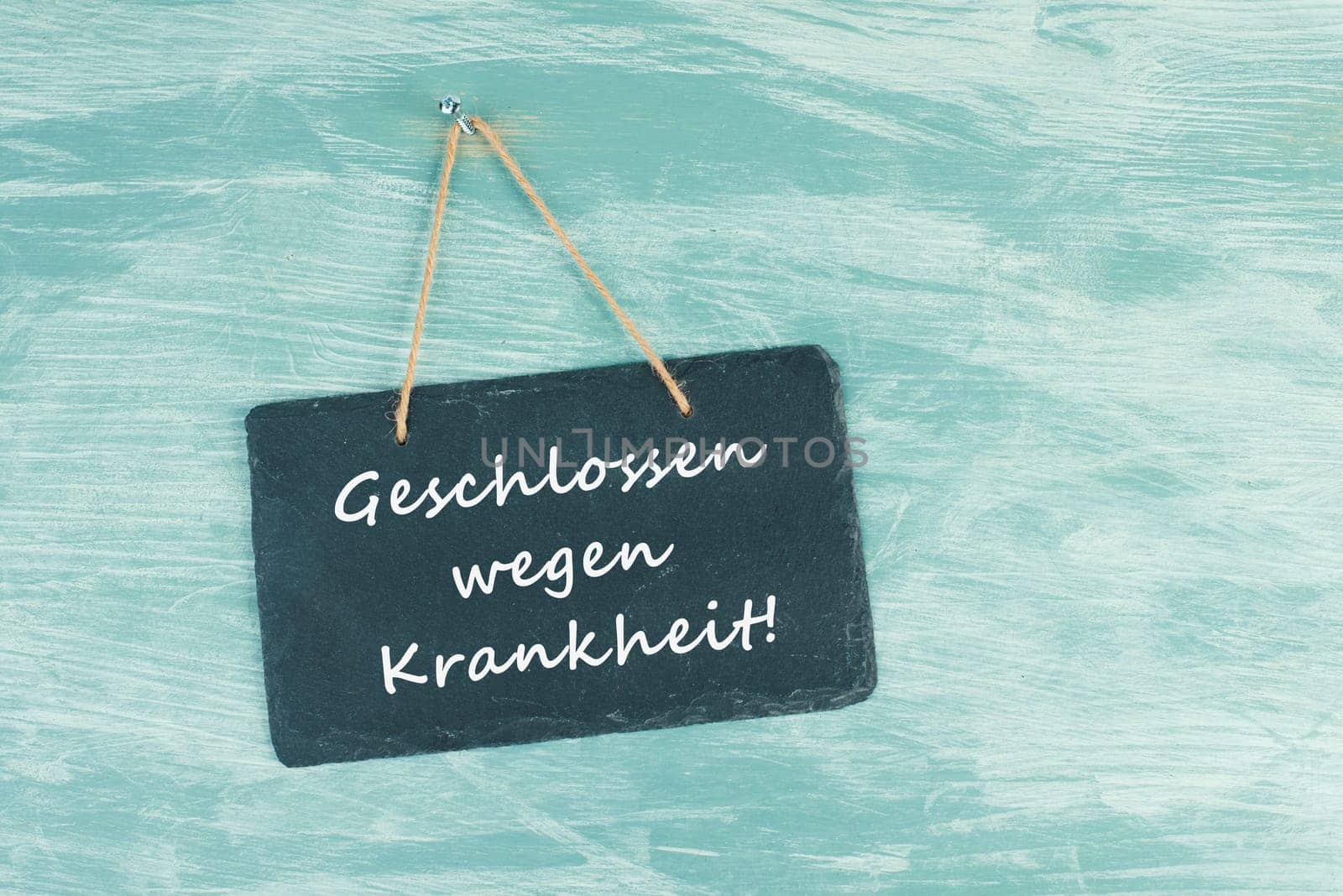 The words closed because of illness are standing in german language on a chalkboard sign, hanging on a blue textured weathered door, concept for business, stores and restaurants