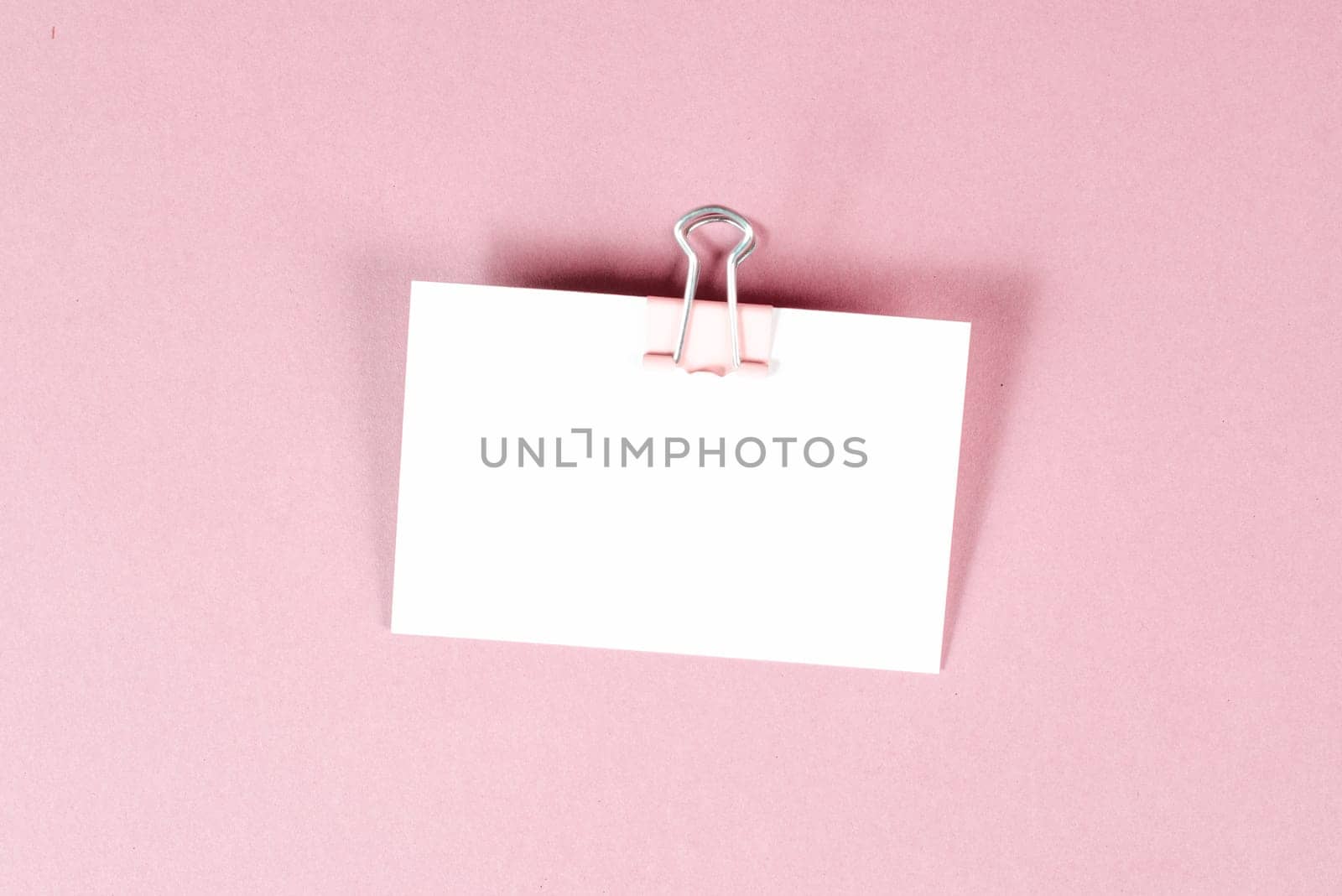 Blank white paper with a paperclip on a pink colored background, copy space for text, reminder or message in the office, communication concept