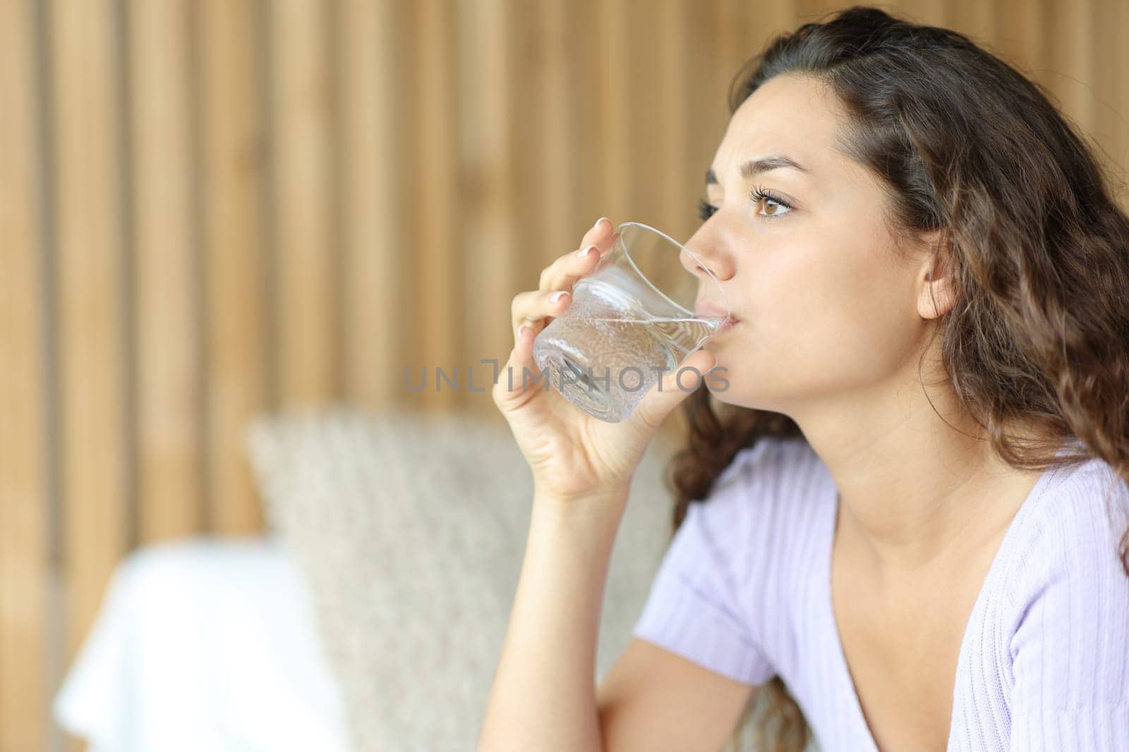 Relaxed woman drinking tap water from glass in a bedroom