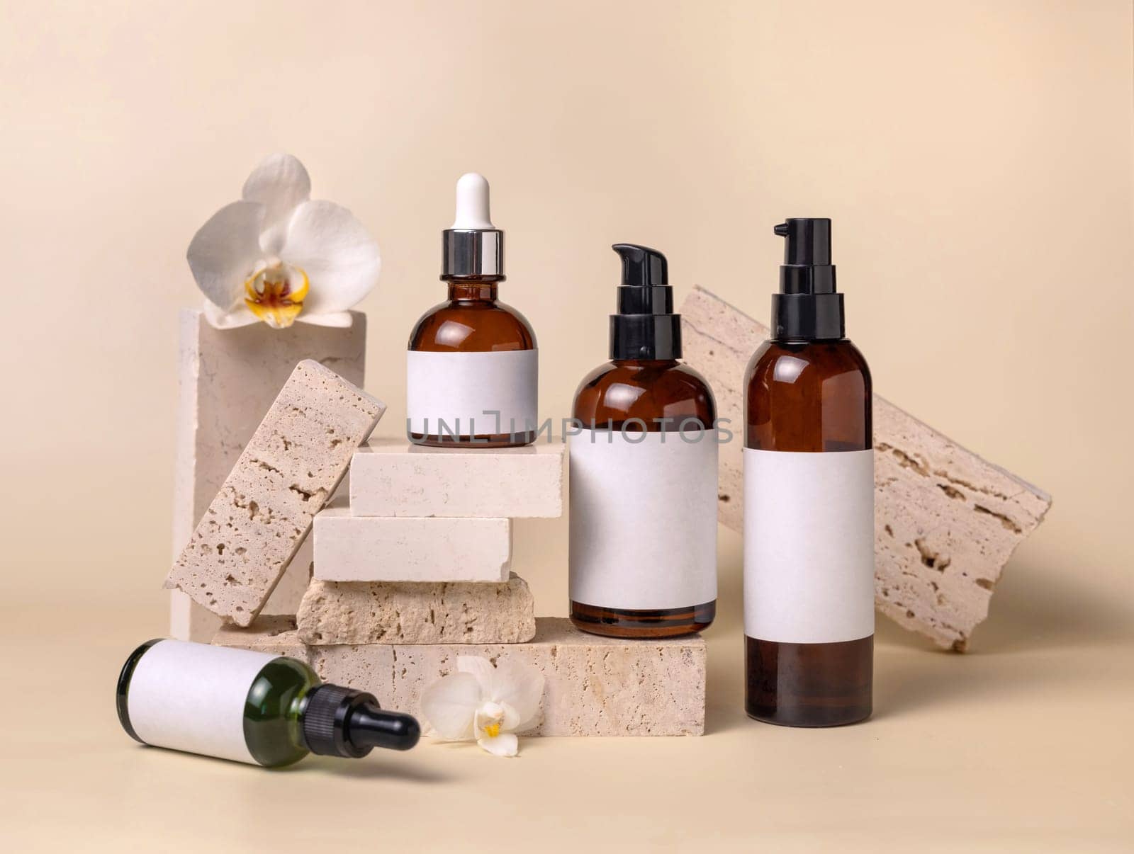 Dark glass bottles with blank labels near white orchid flowers and stones on light beige, close up, package mockup. Skincare beauty products, serum, tonic or lotion. Exotic natural cosmetics..