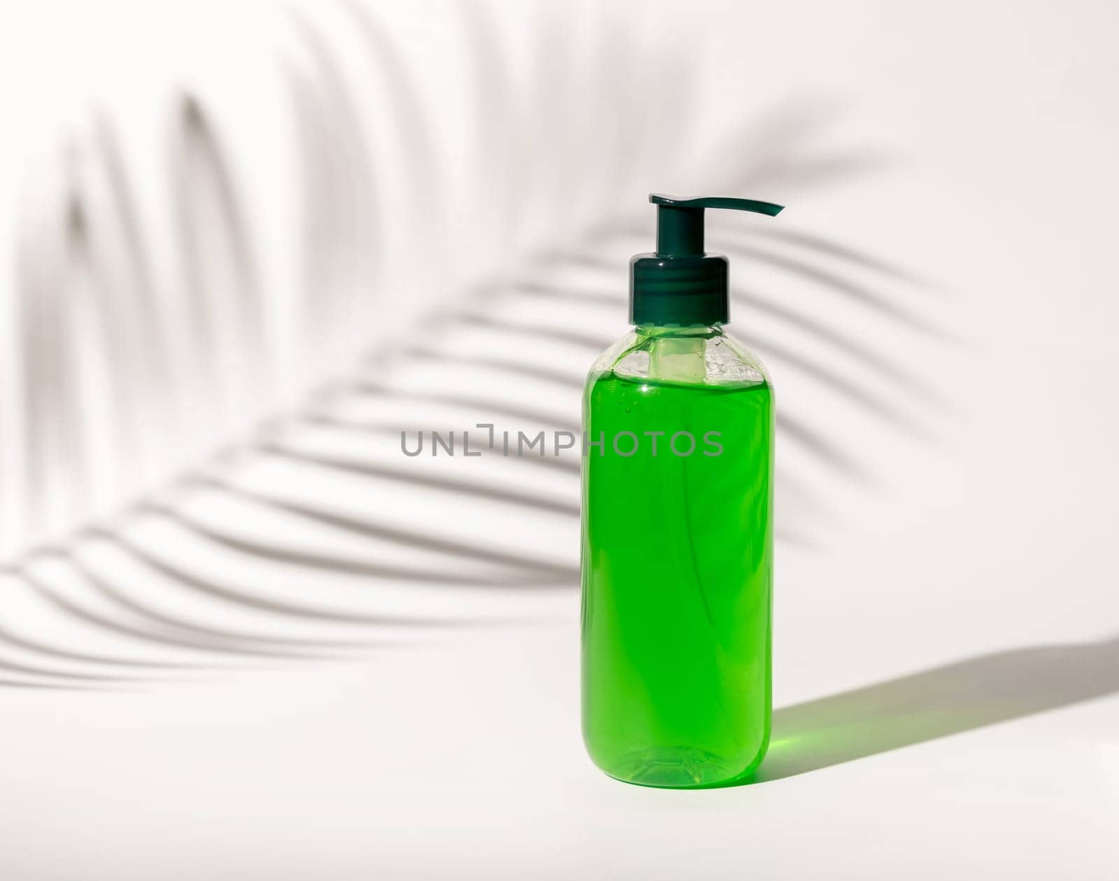 Refillable Cosmetic pump dispenser bottle filled with green liquid on white, Palm leaf hard shadows, close up, mockup. Skincare beauty product, facial cleaner or lotion. Natural cosmetics..