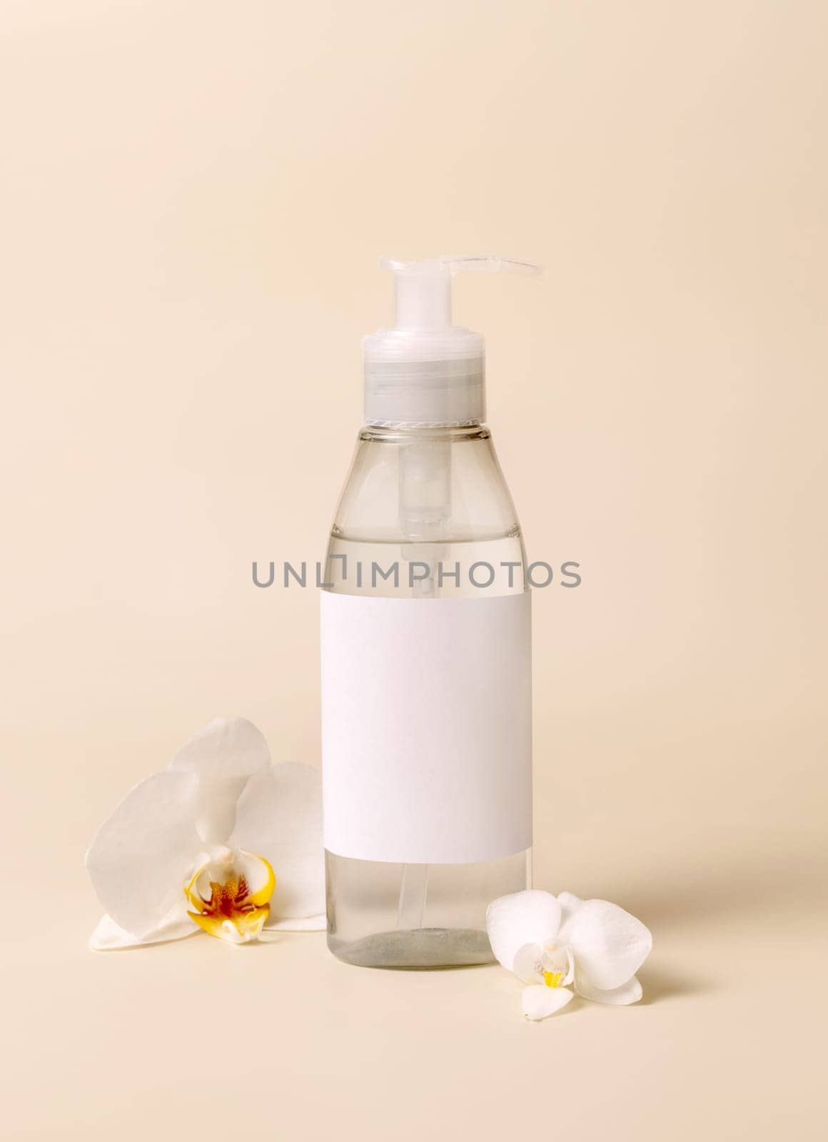 Cosmetic pump dispenser bottle near white orchid flowers on light beige close up, mockup. Skincare beauty product package. Exotic natural cosmetics, pastel minimal composition..