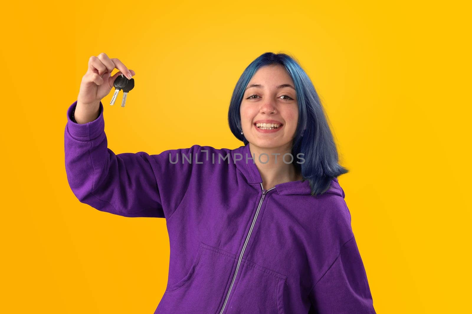 Smiling young woman student with blue hair holding keys over yellow background