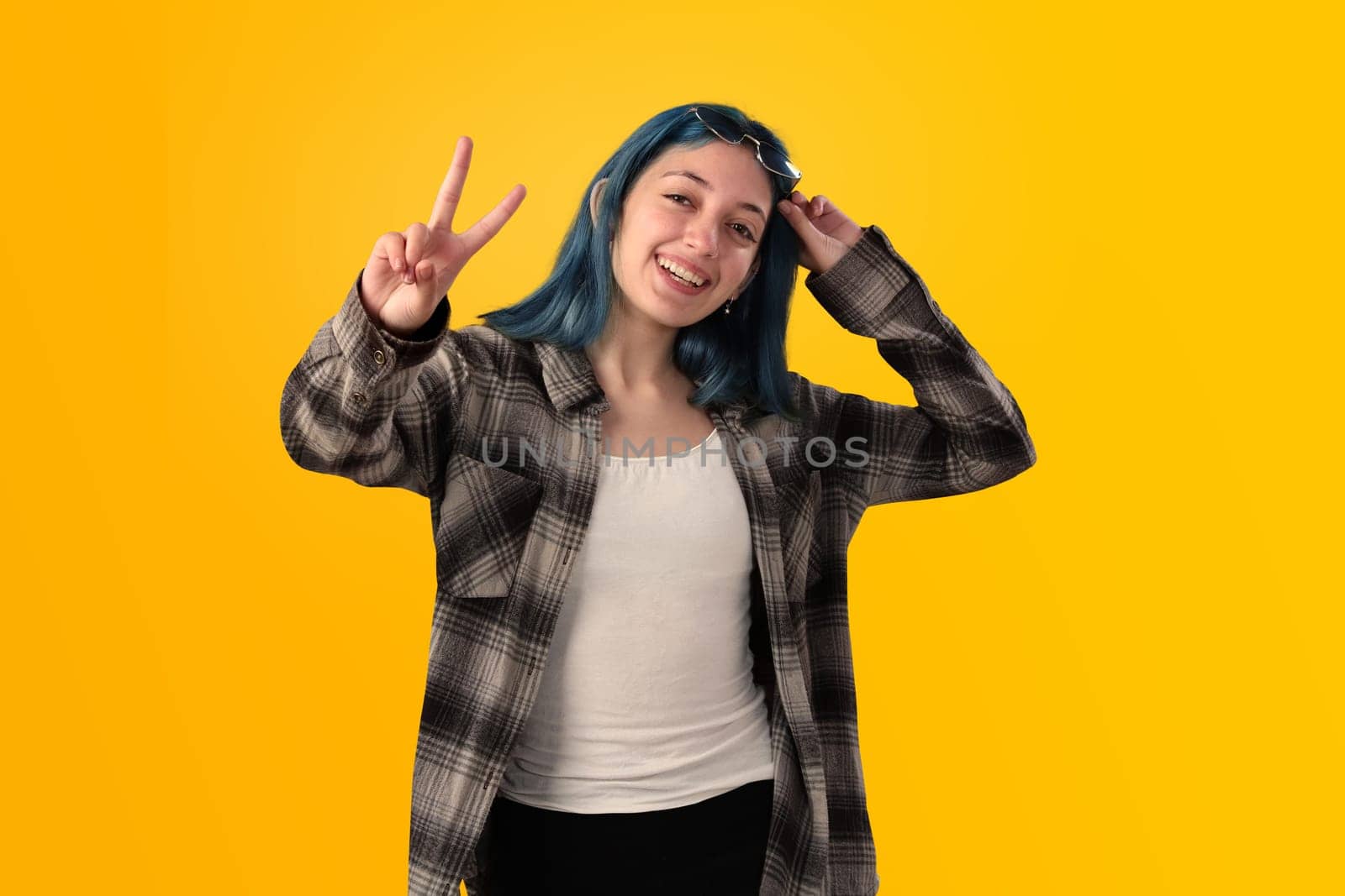 Smiling young woman student with blue hair doing positive gestures with her hands isolated over yellow background