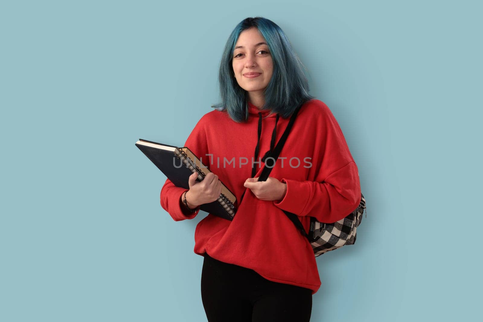 Cute young gilr student with blue hair books and a backpack over a cyan background
