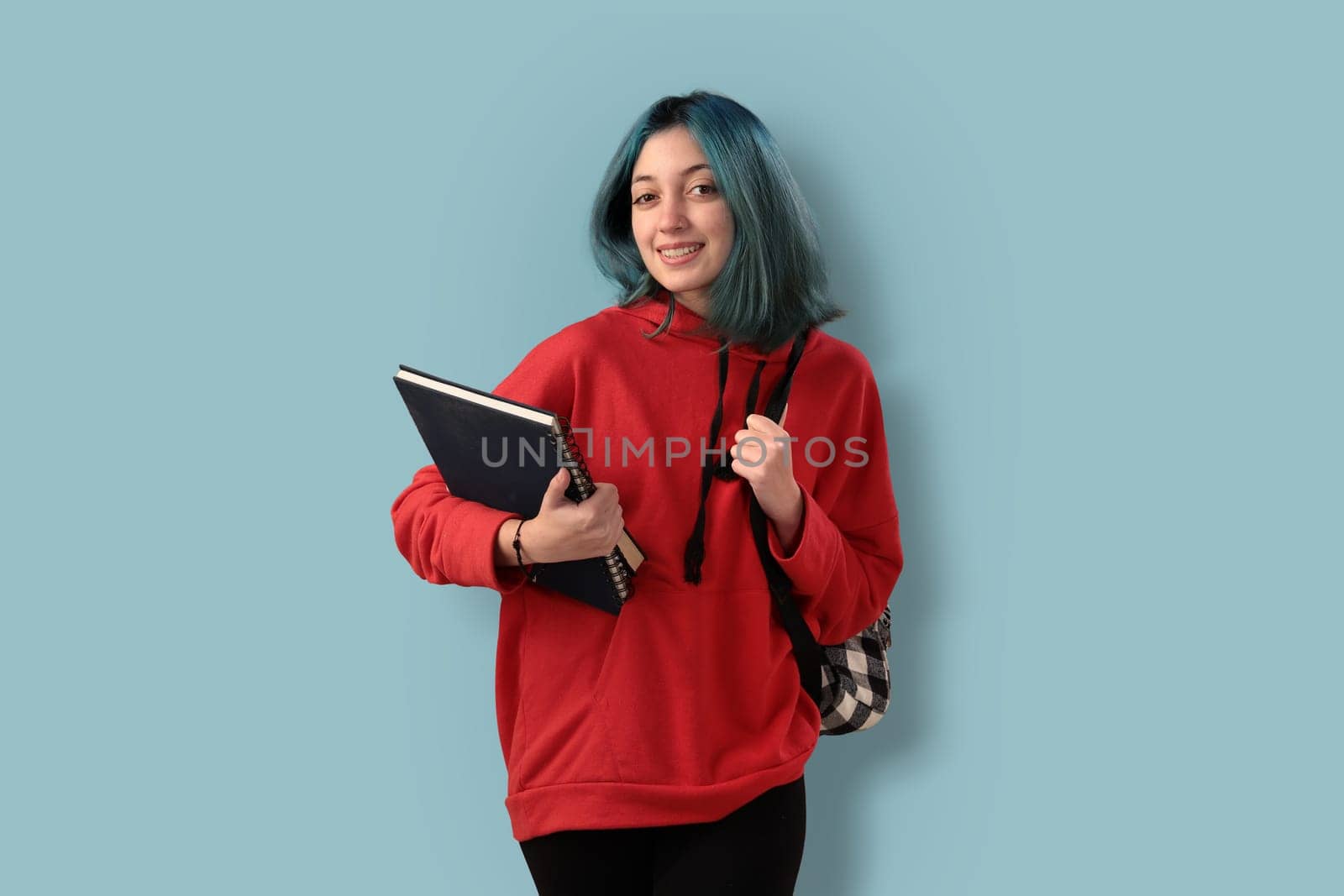 Cute young gilr student with blue hair books and a backpack over a cyan background