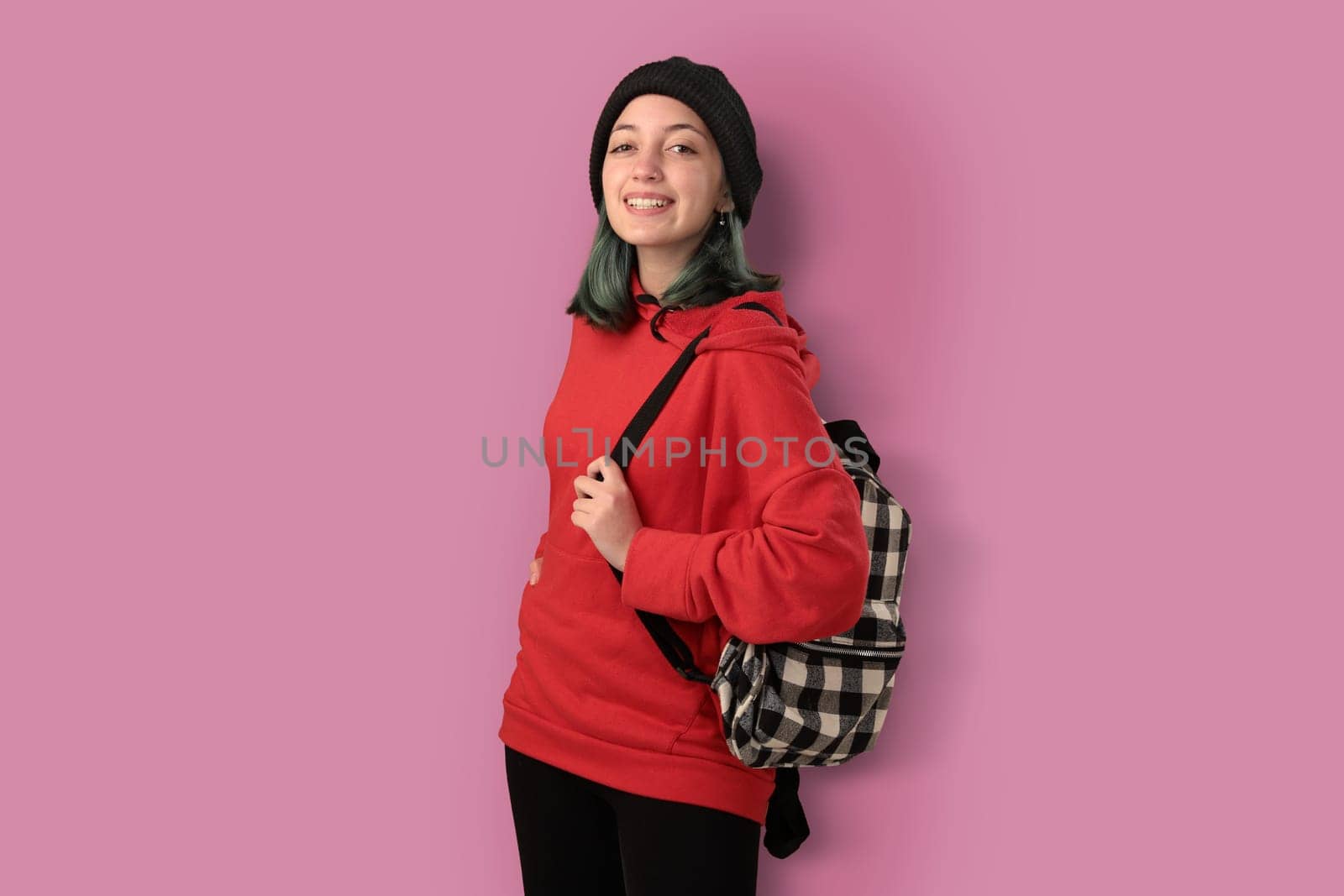 Cute young gilr student with blue hair and a backpack isolated over pink background