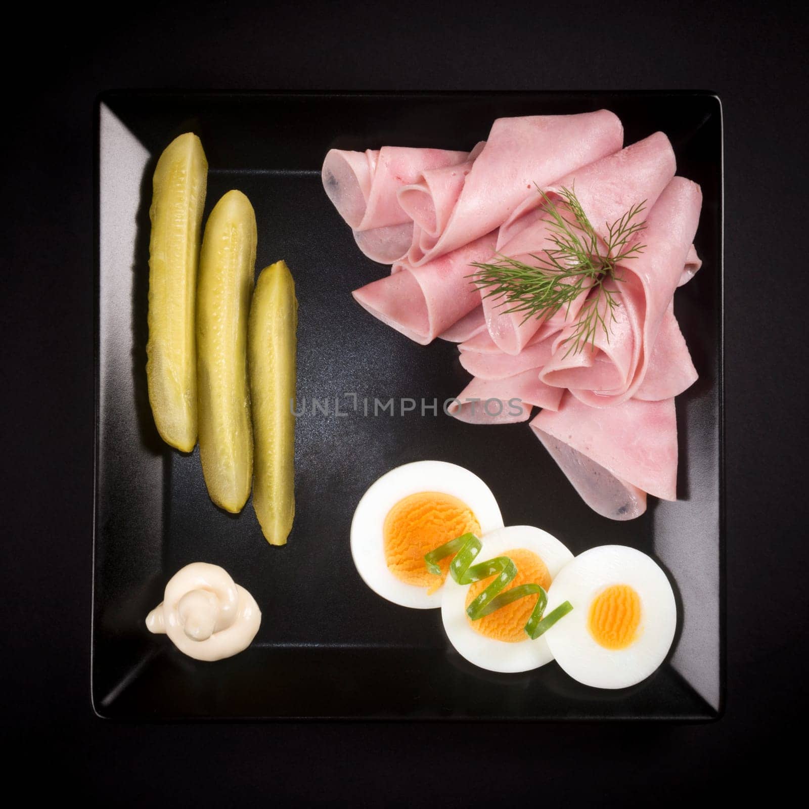 Elegant cold appetizer, ham, egg and pickle on black plate on black background in gourmet restaurant.