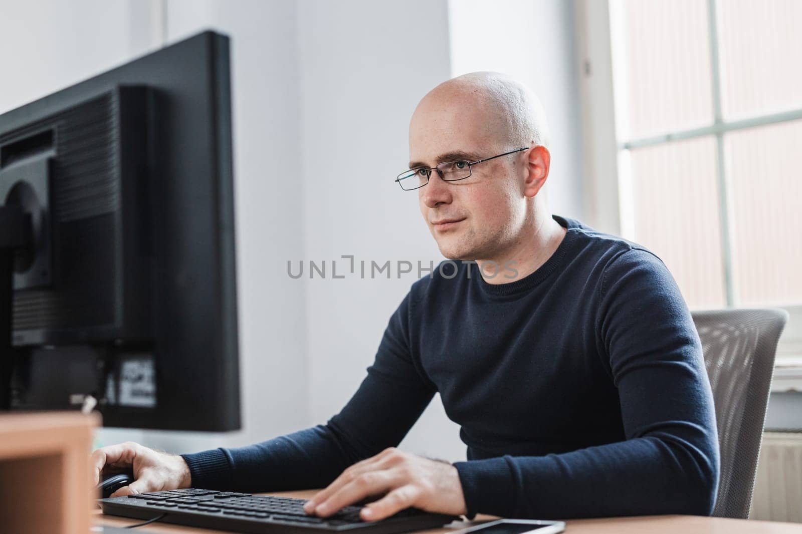 Young Entrepreneur Wearing Eyeglasses Sitting at his Table Inside the Office, Looking at the Report on his Computer Screen
