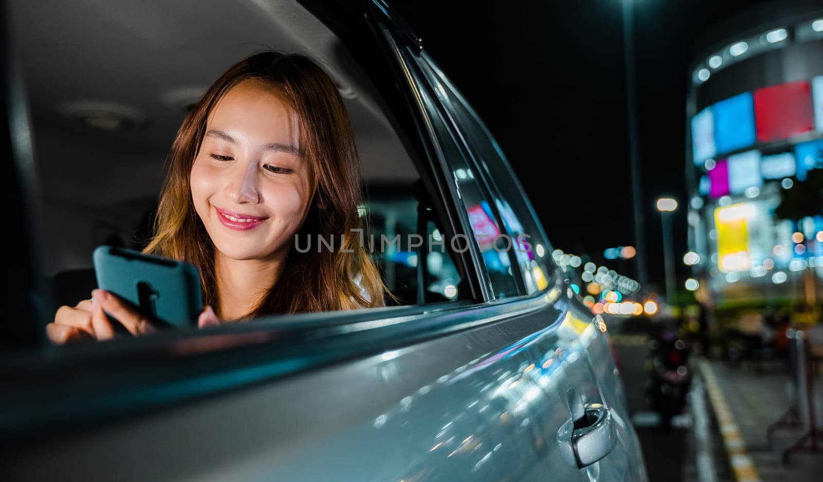 Happy beautiful woman texting smartphone sitting back seat her car in urban, Asian businesswoman commuting from office in Taxi backseat with mobile phone on road in city at night after late work