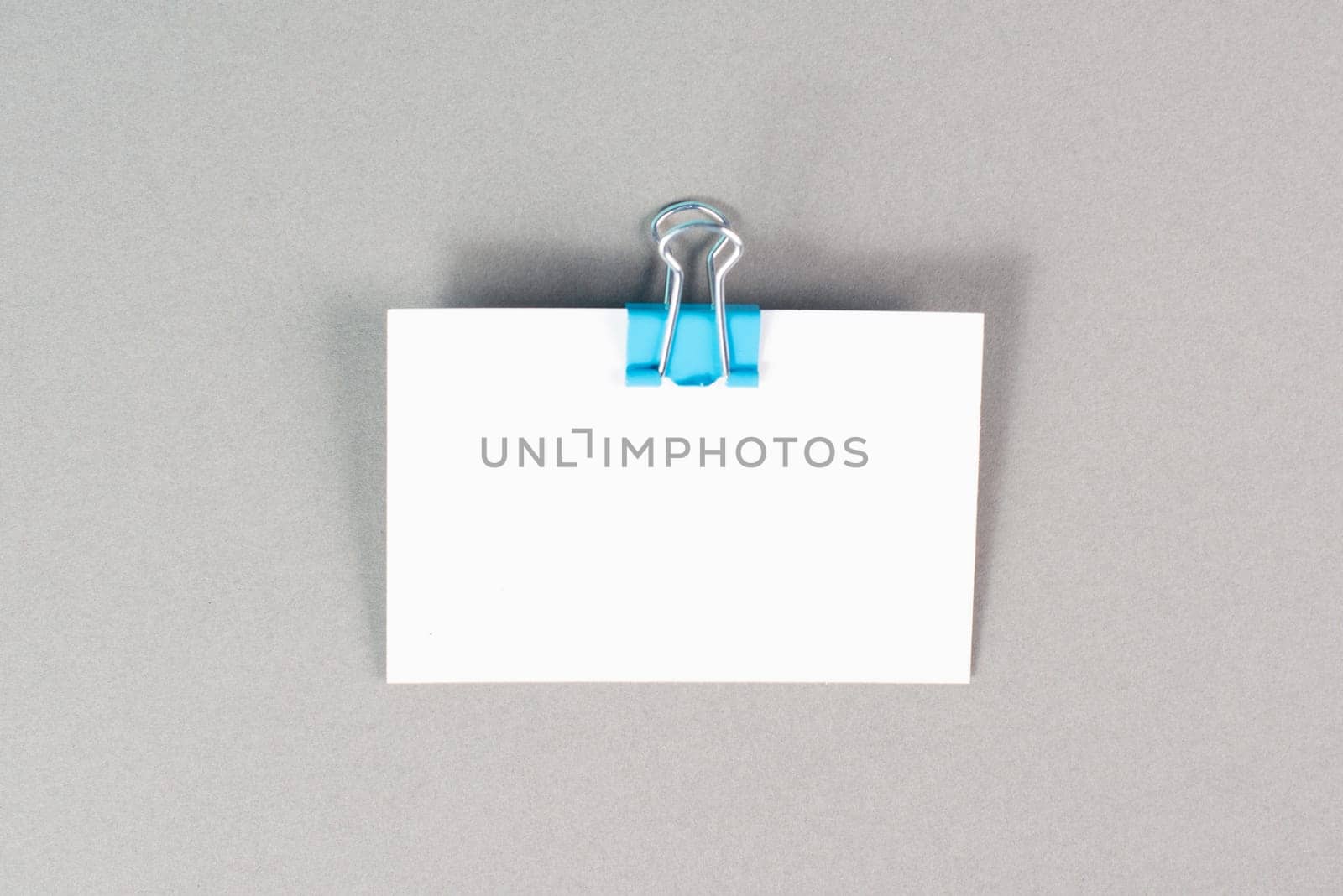 Blank white paper with a paperclip on a graycolored background, copy space for text, reminder or message in the office, communication concept