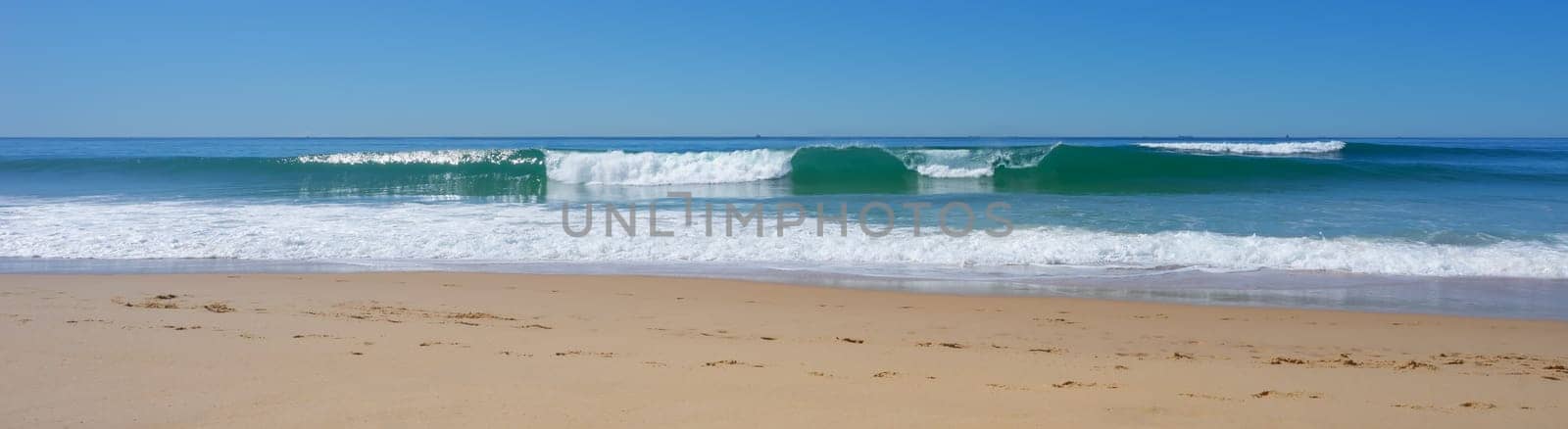 Panorama of surf waves rolling in to the beach on a calm, sunny, winter day.