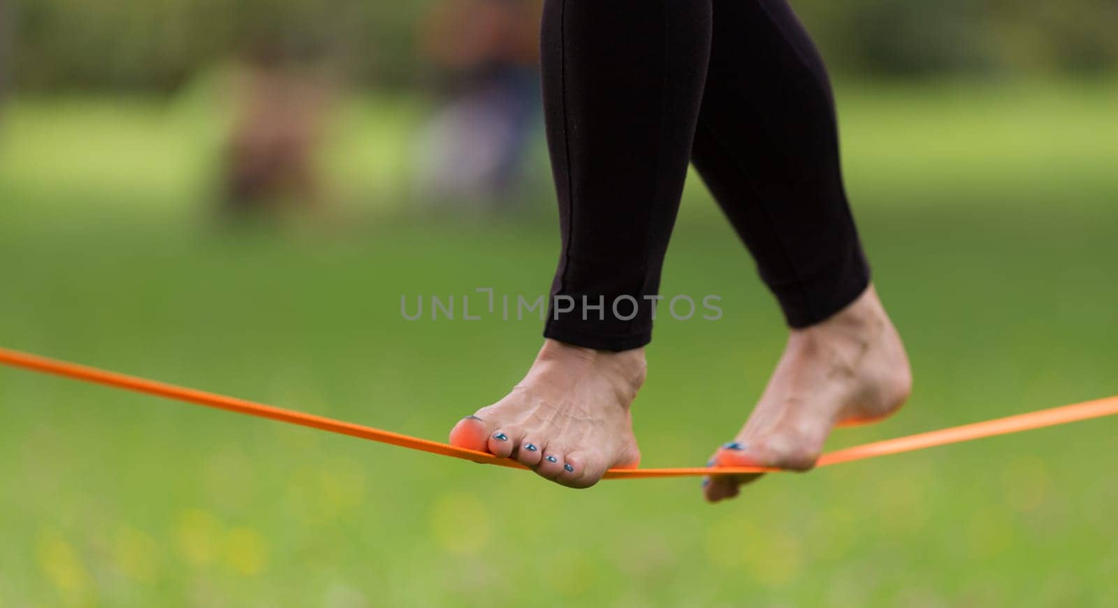 Lady practising slack line in the city park. Slacklining is a practice in balance that typically uses nylon or polyester webbing tensioned between two anchor points.
