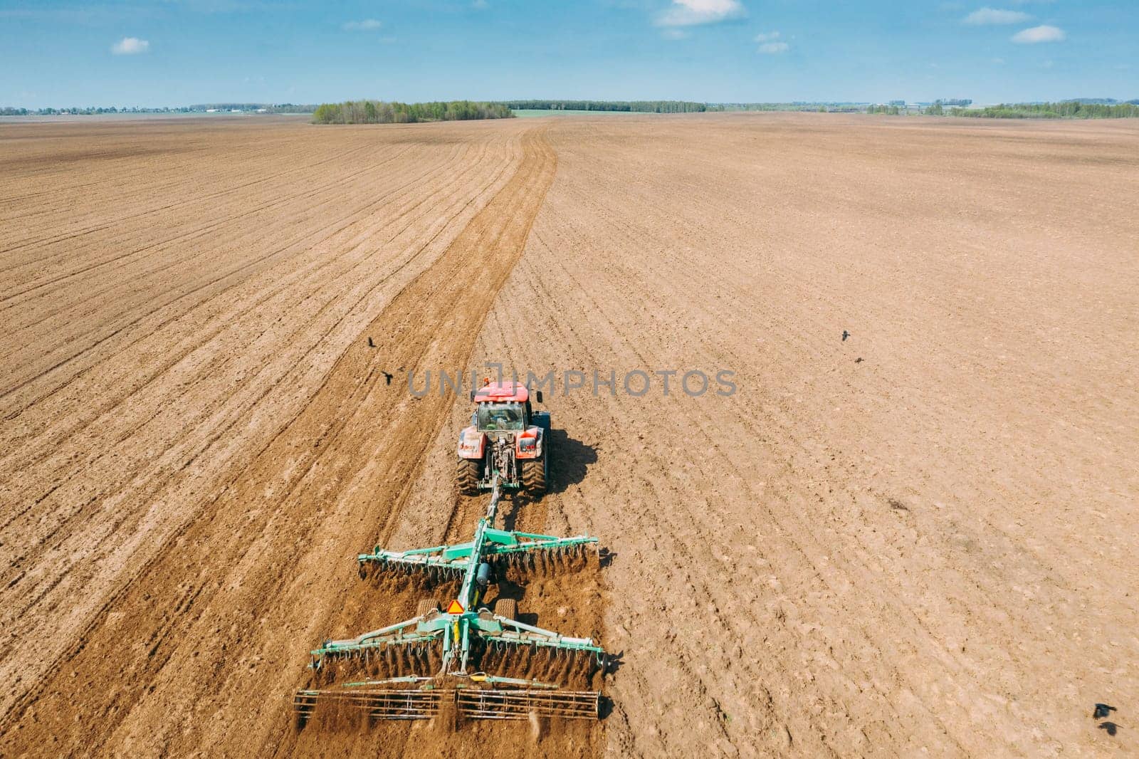Aerial View. Tractor Plowing Field In Spring Season. Beginning Of Agricultural Spring Season. Cultivator Pulled By A Tractor In Countryside Rural Field Landscape.