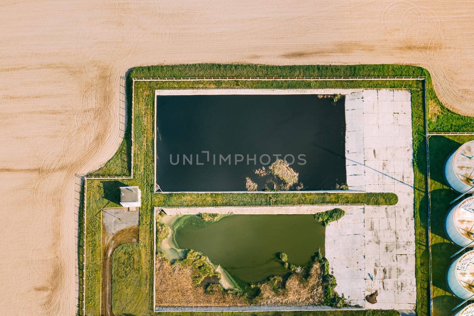 Aerial View Of Retention Basins, Wet Pond, Wet Detention Basin Or Stormwater Management Pond Near Biogas Bio-gas Plant From Pig Farm. Artificial Pond With Vegetation Around Perimeter