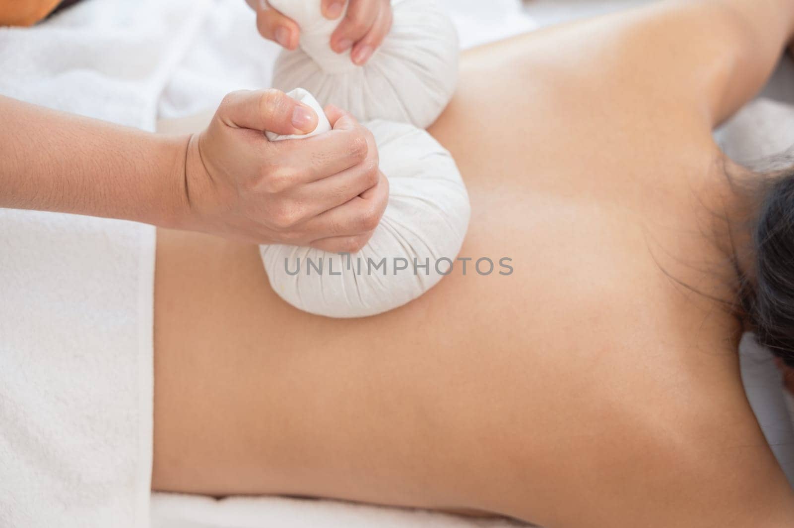 Masseur hands make back massage with Thai herbal compress for young woman on massage table