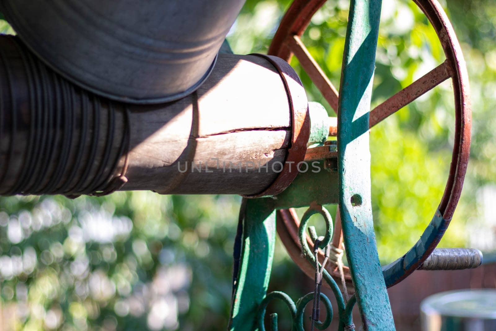 A well with a bucket in a European village. Sunny day. Metal bucket for a water well. Detail of a well with a tin bucket in the countryside. Decorating the garden with vintage items