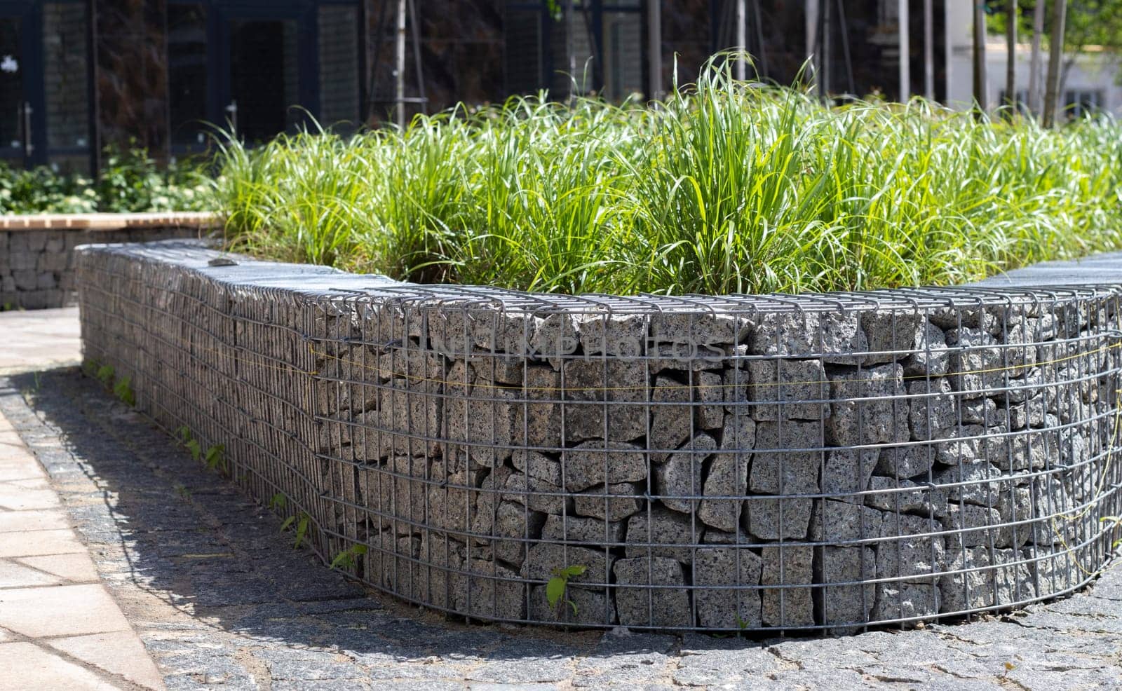 Basket support wall made of granite gabion. Gabions in the garden. Modern Gabion fence with stones in wire mesh. Gabion wire mesh fencing with natural stone and shrubs