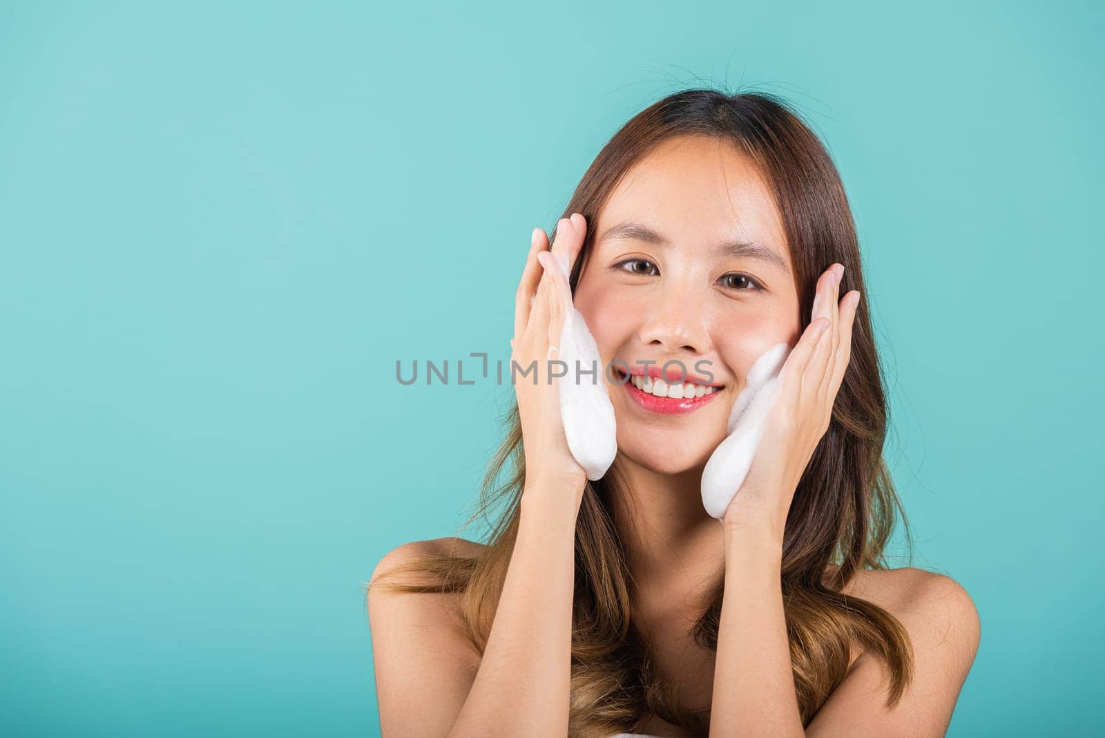 Asian woman face wash exfoliate scrub soap foam with skincare cleansing, Portrait beautiful female smile applies foaming cleanser healthy skin, Studio isolated on blue background, beauty skincare