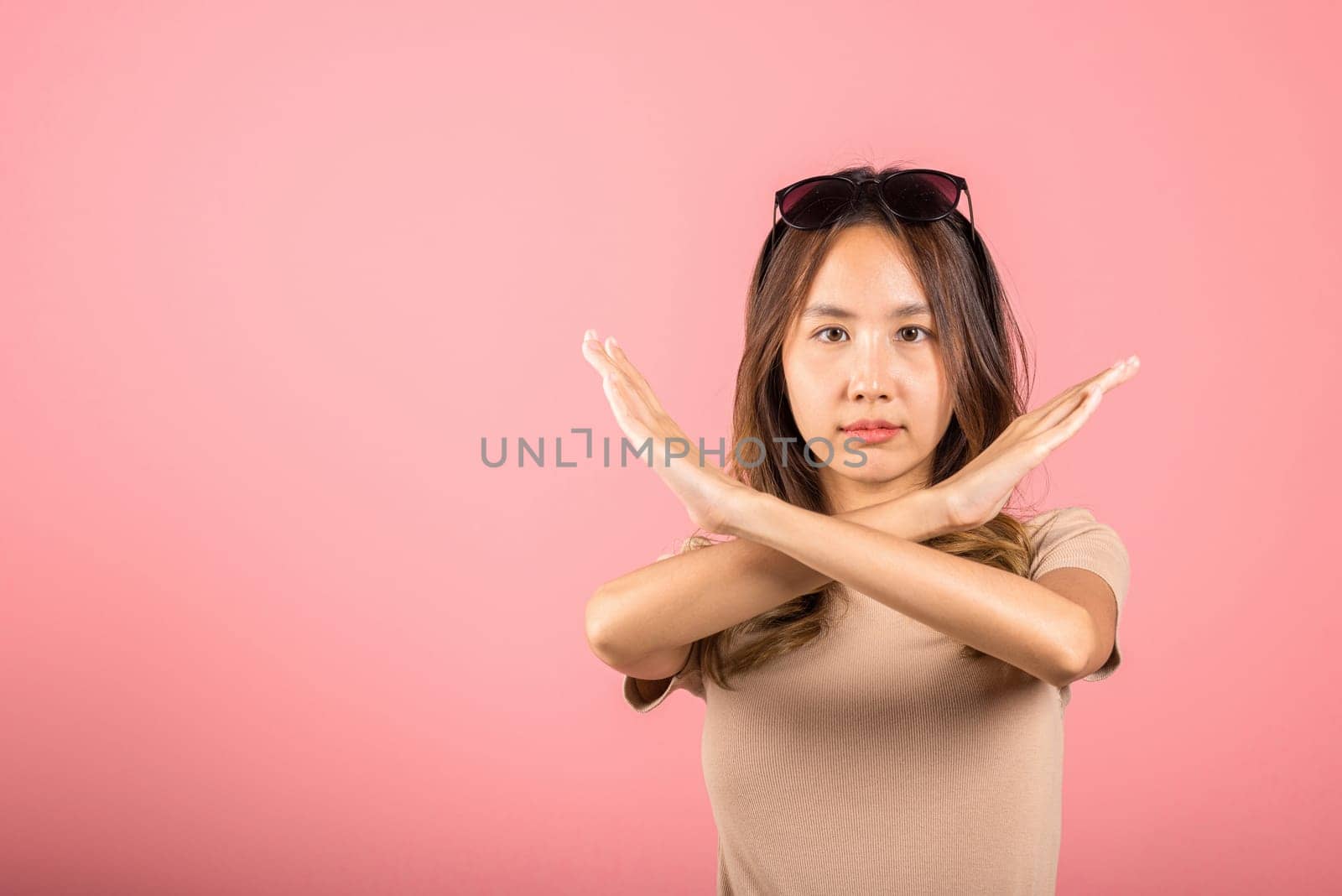 Portrait Asian beautiful young woman unhappy or confident standing holding two cross arms say no X stop sign, studio shot isolated pink background, Thai female pose reject gesture with copy space