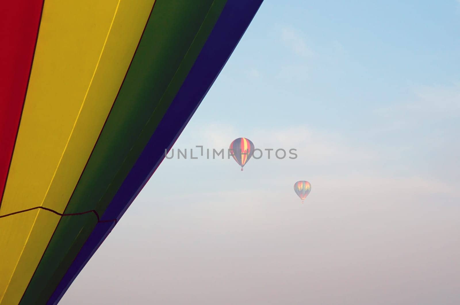 Two hot air balloons can be seen high up in the sky and partially obscured by the fog in the air, The side of another balloon fills the side of the image up close.