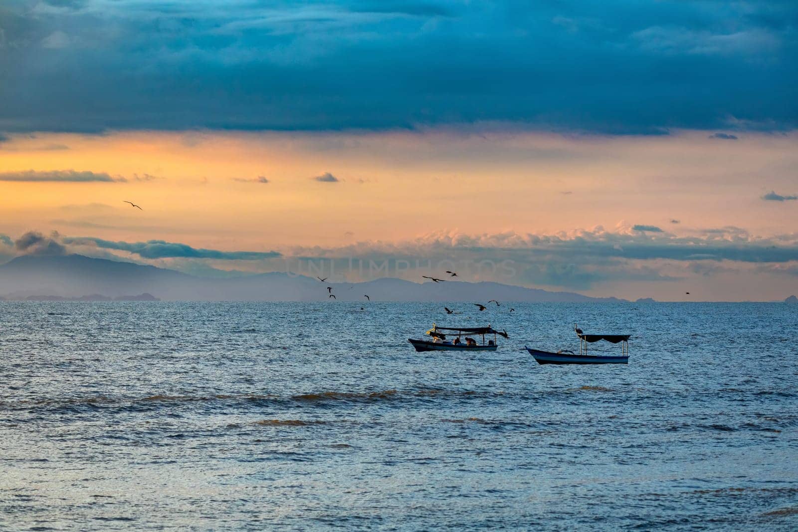 Evening view of the Pacific Coast of Tarcoles in Carara with sunset and glittering waves . Idyllic sunset landscape with fishing boats. Tarcoles, Costa Rica. Pura Vida concept.